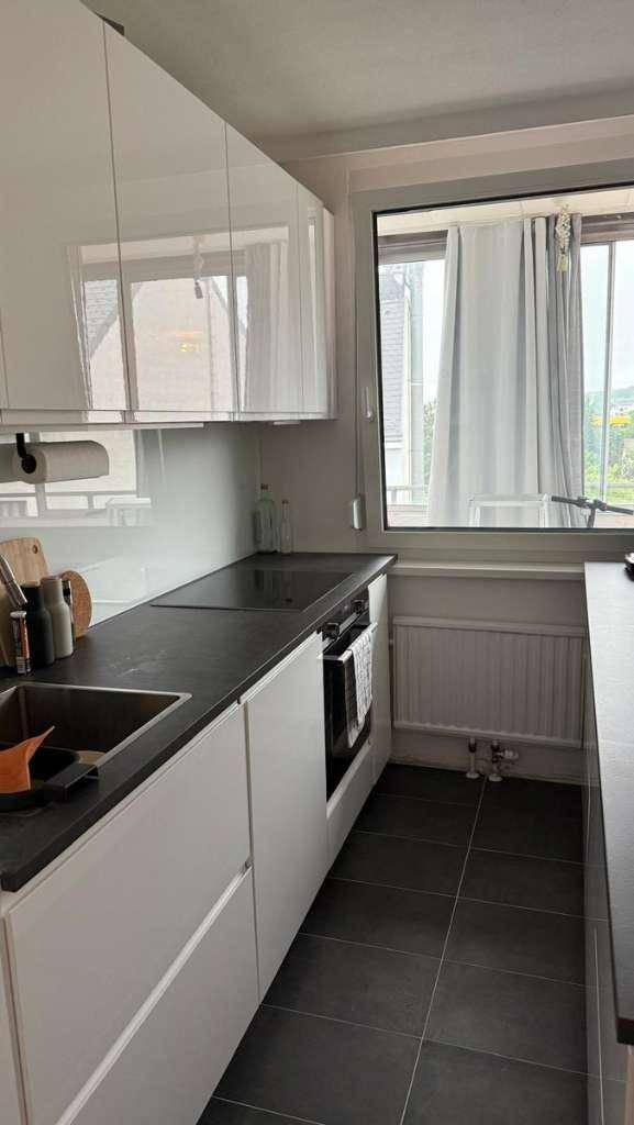 Helle Küche mit weißen Schränken, dunkler Arbeitsplatte und Fenster mit Blick ins Grüne.