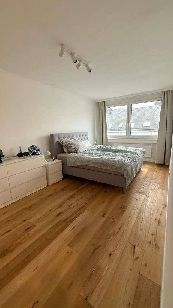 Gemütliches Schlafzimmer mit Holzboden, großem Bett und Fenster mit viel Tageslicht.