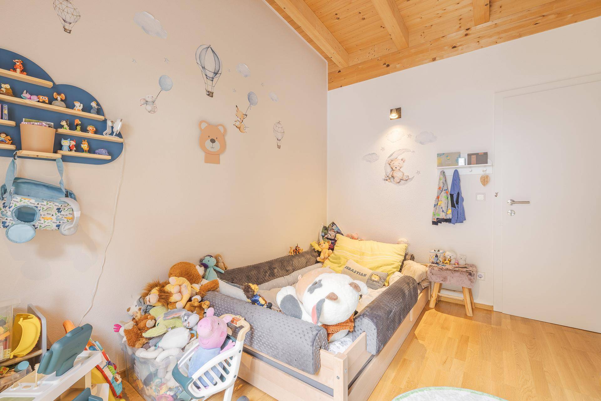 Helles Kinderzimmer mit Holzbalkendecke, Holzboden und vielen Kuscheltieren, ein Spielparadies.