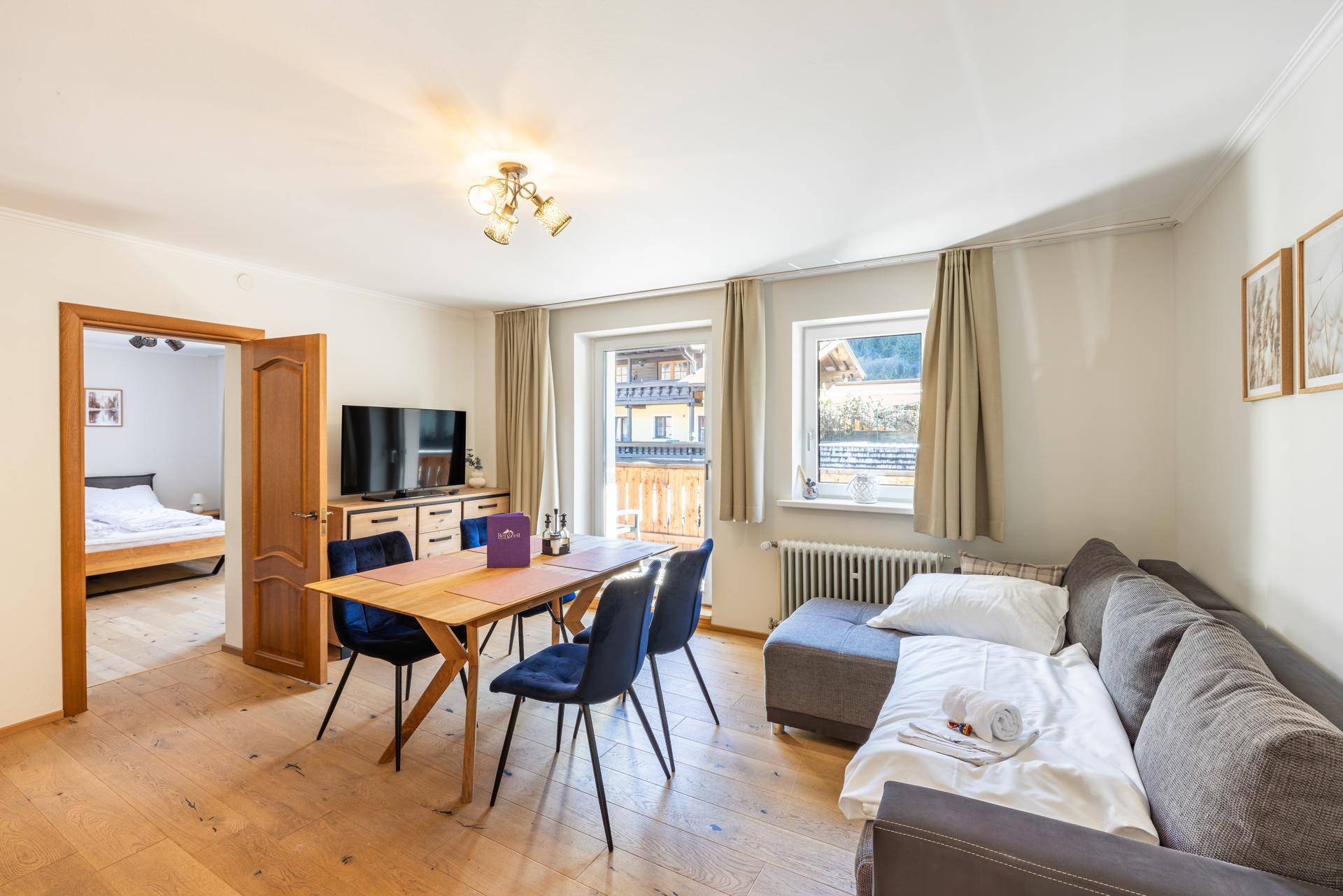 Offener Wohn- und Essbereich mit Holzboden, Esstisch und Blick in ein angrenzendes Schlafzimmer.