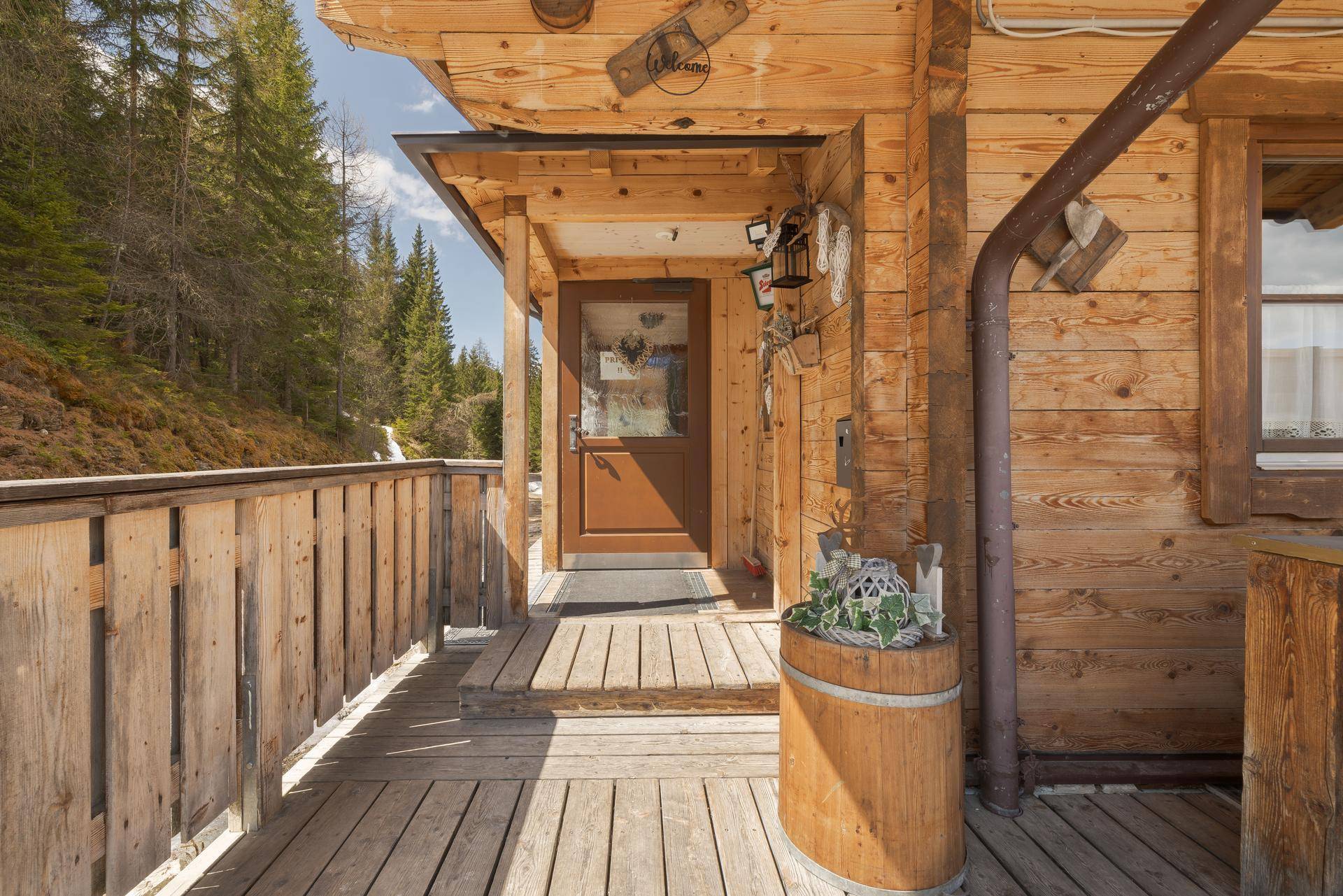 Detailansicht des Eingangs auf der Holzterrasse mit rustikaler Dekoration und umgebender Waldlandschaft.