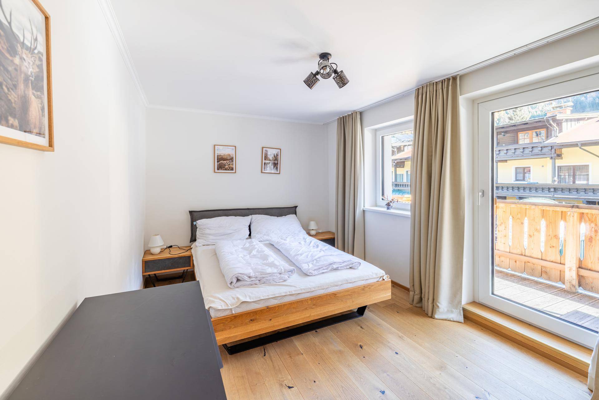 Schlafzimmer mit Doppelbett, Holzboden und Zugang zu einem sonnigen Balkon.