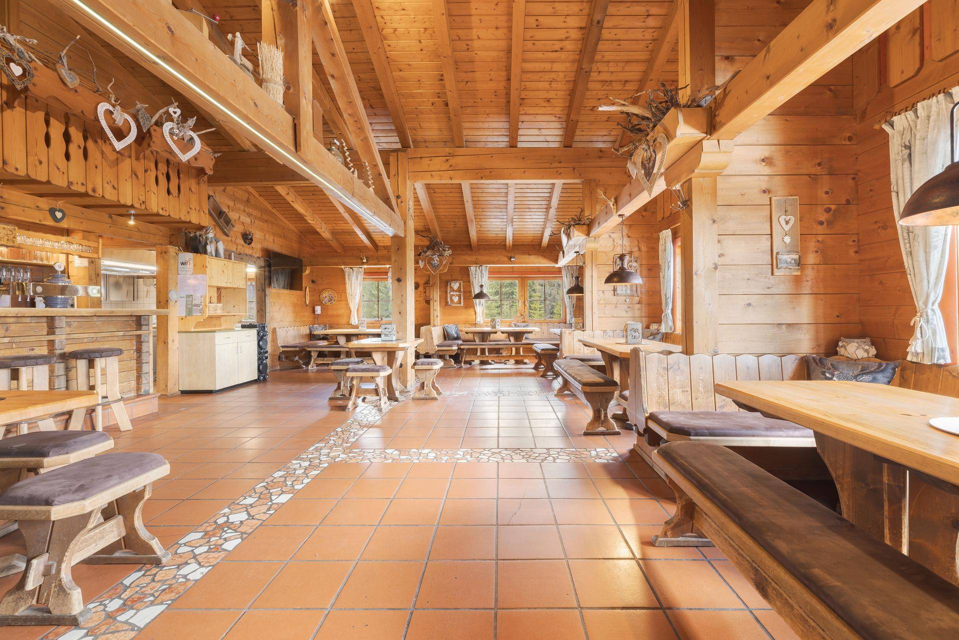 Geräumiger Speisesaal mit rustikalen Holzbänken und Tischen, Terrakottafliesen und einer gemütlichen Bar.