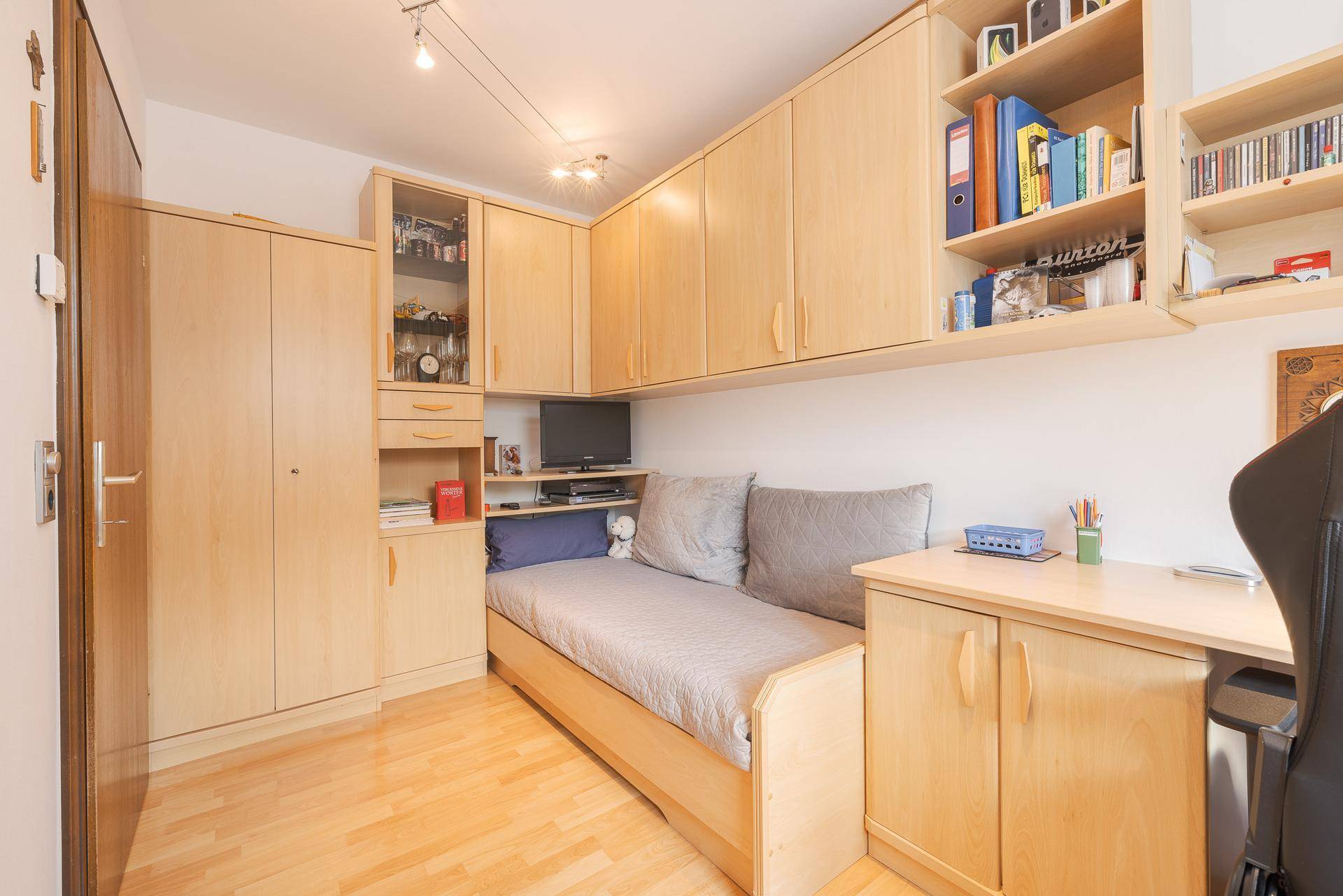 Funktionales Arbeitszimmer mit integrierten Schränken, Tagesbett und hellem Holzfußboden.