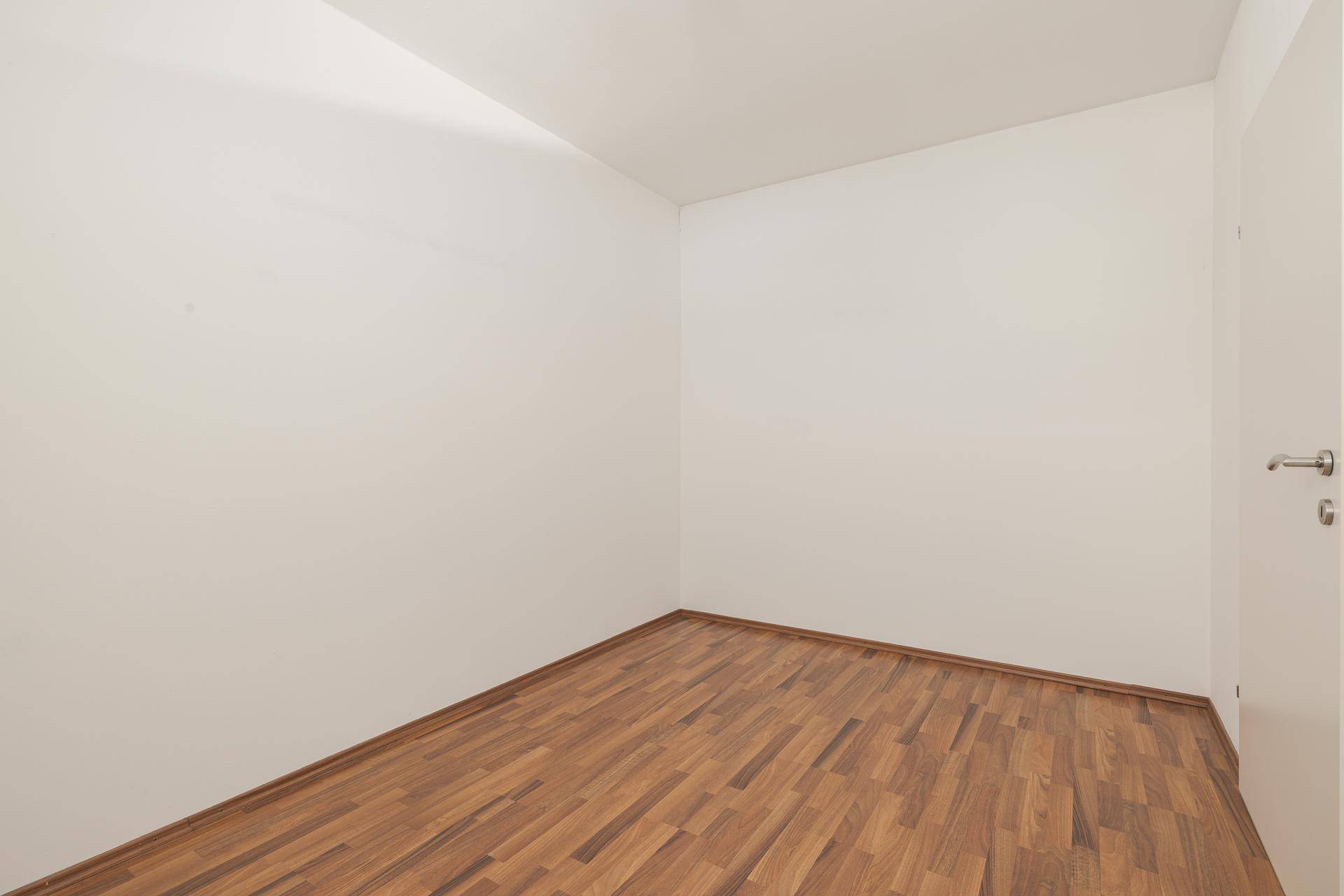 Kleines, leeres Zimmer mit Laminatboden und weißen Wänden, ideal als Kinder- oder Arbeitszimmer.