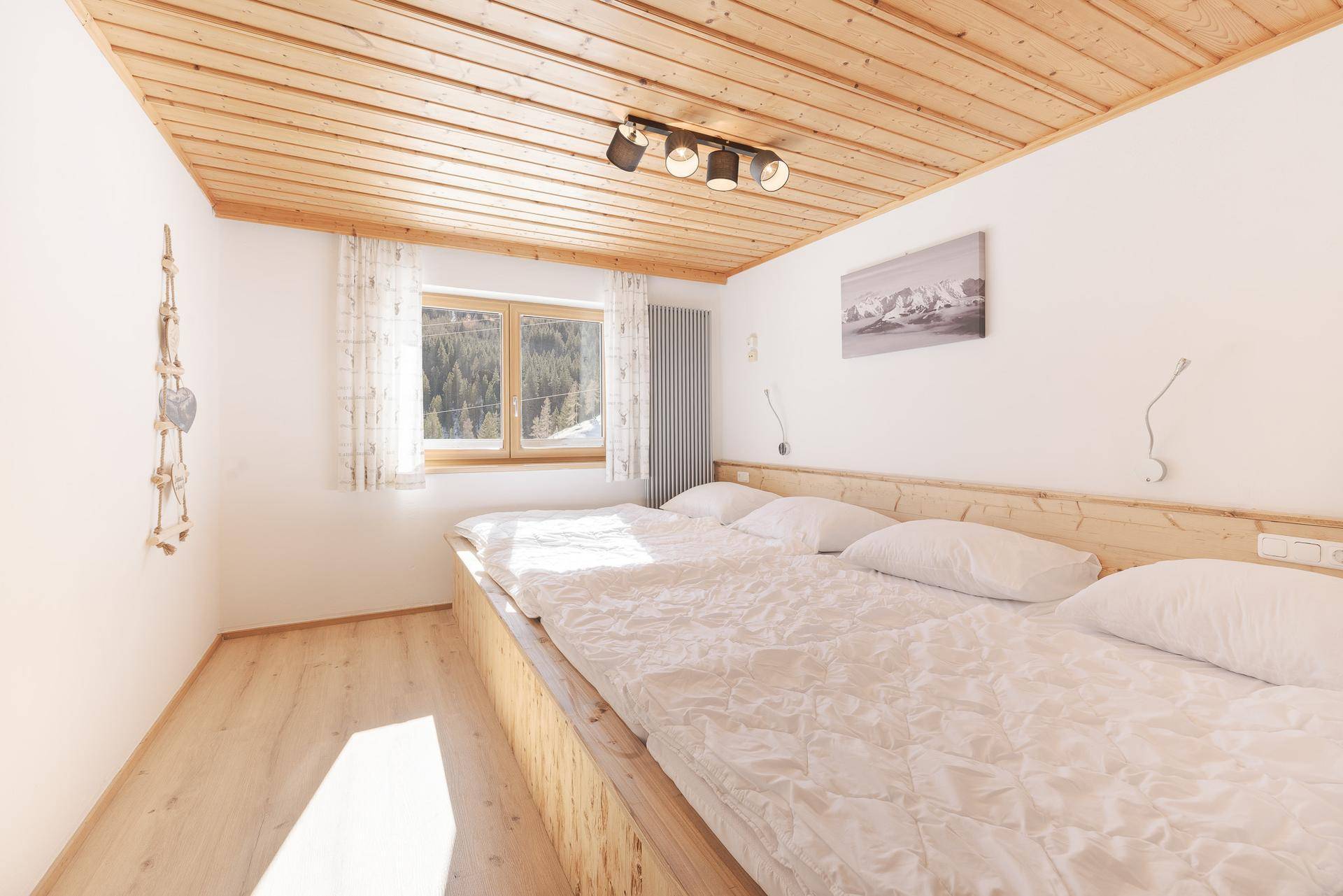 Helles Schlafzimmer mit Doppelbett, Holzdecke und Blick auf die verschneite Landschaft.