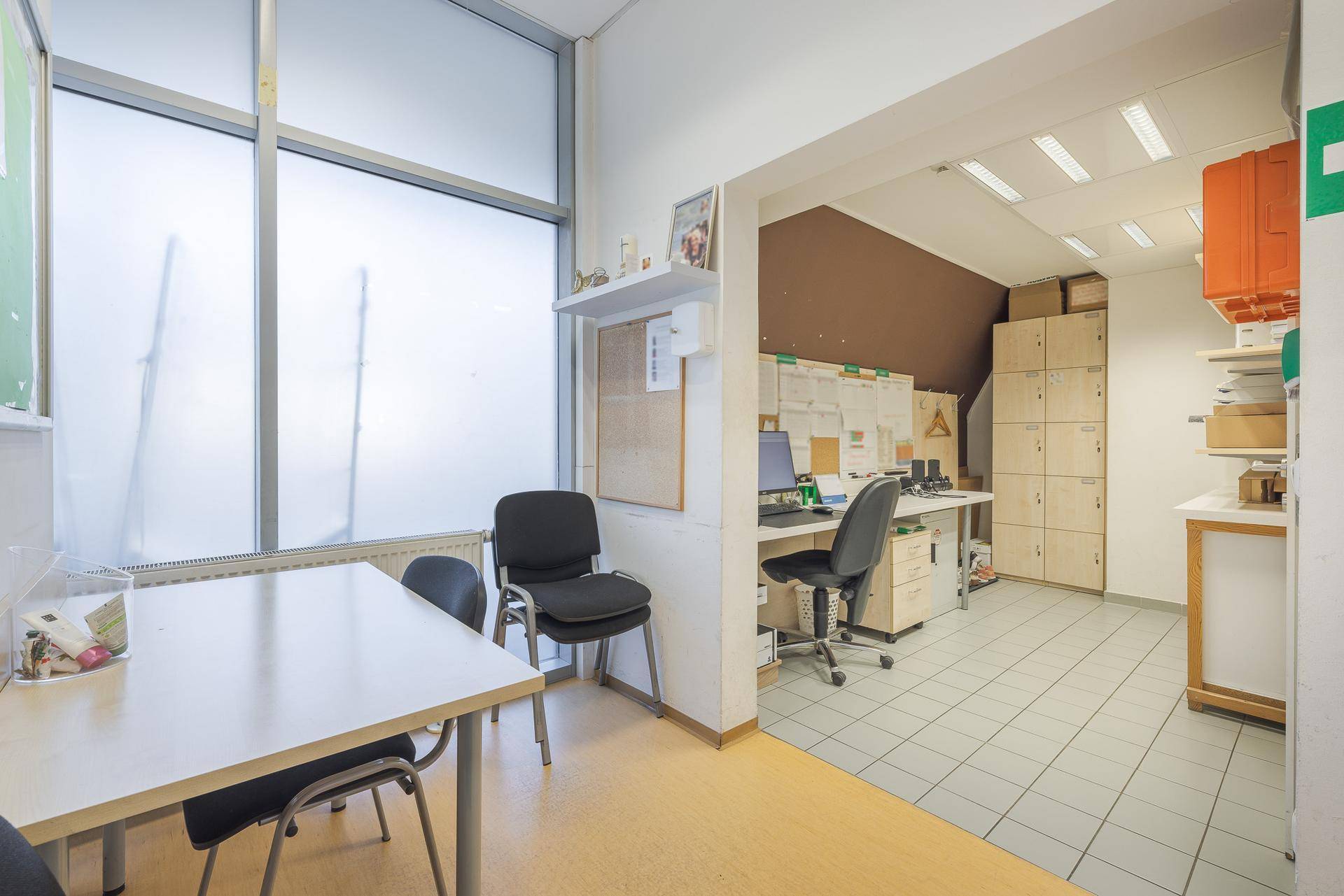 Büro- und Pausenraum mit Schreibtischen, Stühlen und einem großen Fenster.