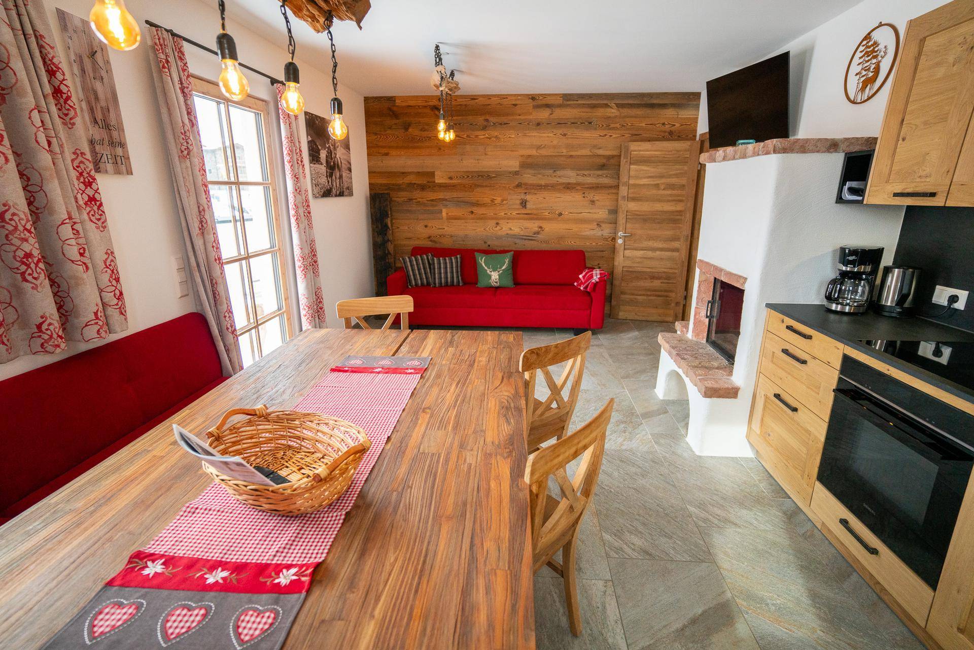 Offener Wohnbereich mit Holzwand, rotem Sofa, Esstisch und integrierter Küche, schafft eine warme Atmosphäre.