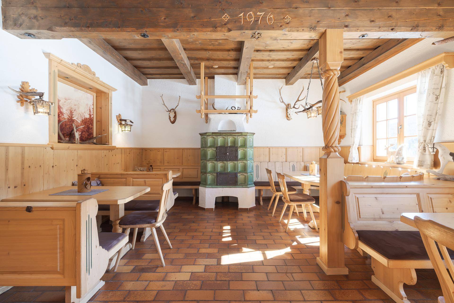 Gemütlicher Essbereich mit Kachelofen, Holzbalkendecke und traditionellen Holzmöbeln.