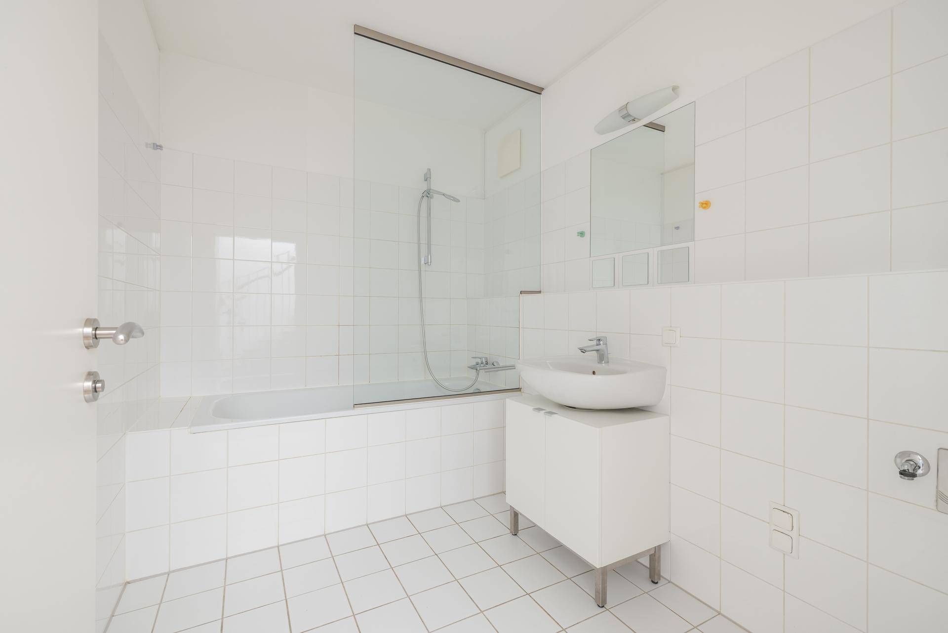 Modernes Badezimmer mit weißen Fliesen, Badewanne mit Duschabtrennung und einem Waschbecken.