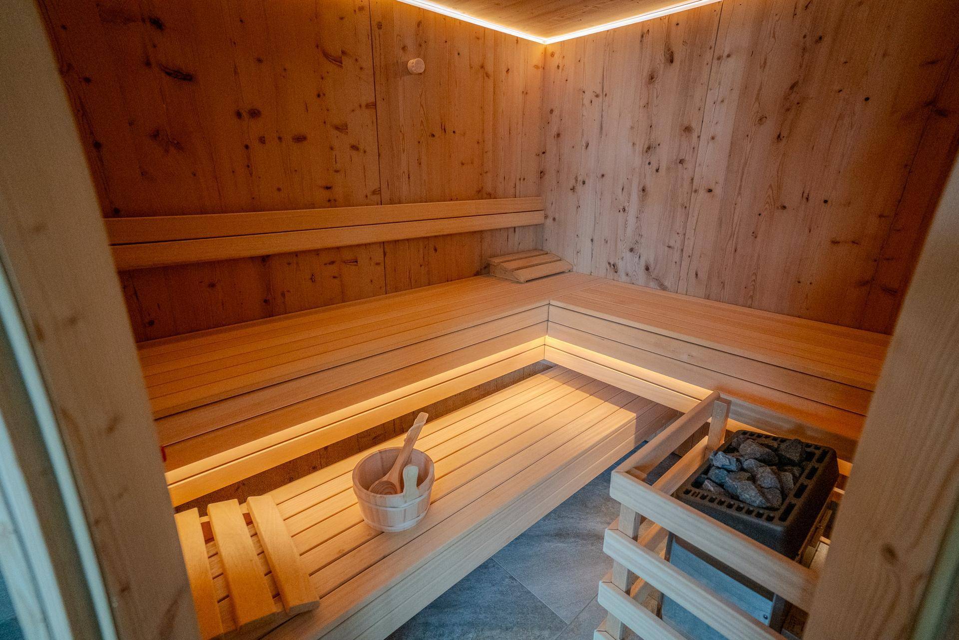 Innenansicht der Holzsauna mit Bänken und Beleuchtung, perfekt für entspannende Momente.