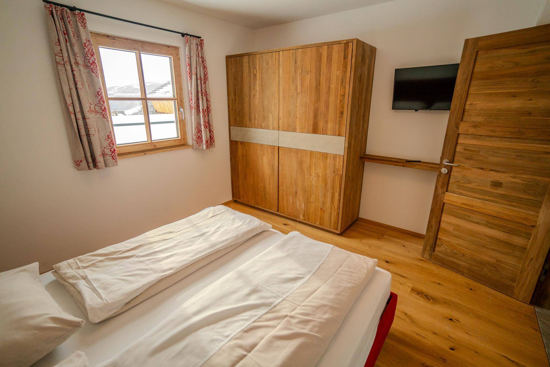 Gemütliches Schlafzimmer mit Doppelbett, Holzschrank und Fensterblick, ideal für erholsame Nächte.