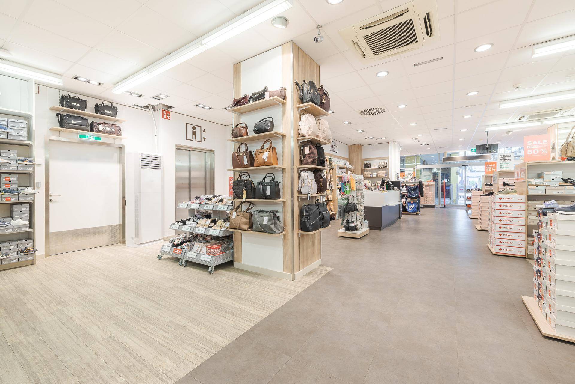 Verkaufsfläche eines Schuhgeschäfts mit Aufzug und verschiedenen Produktpräsentationen.