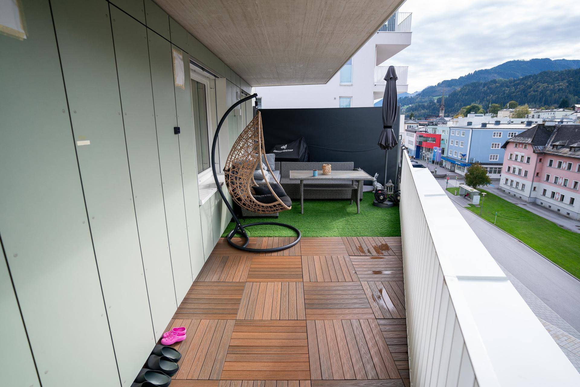 Gemütlicher Balkon mit Holzboden, Hängesessel und Blick auf die umliegende Berglandschaft.