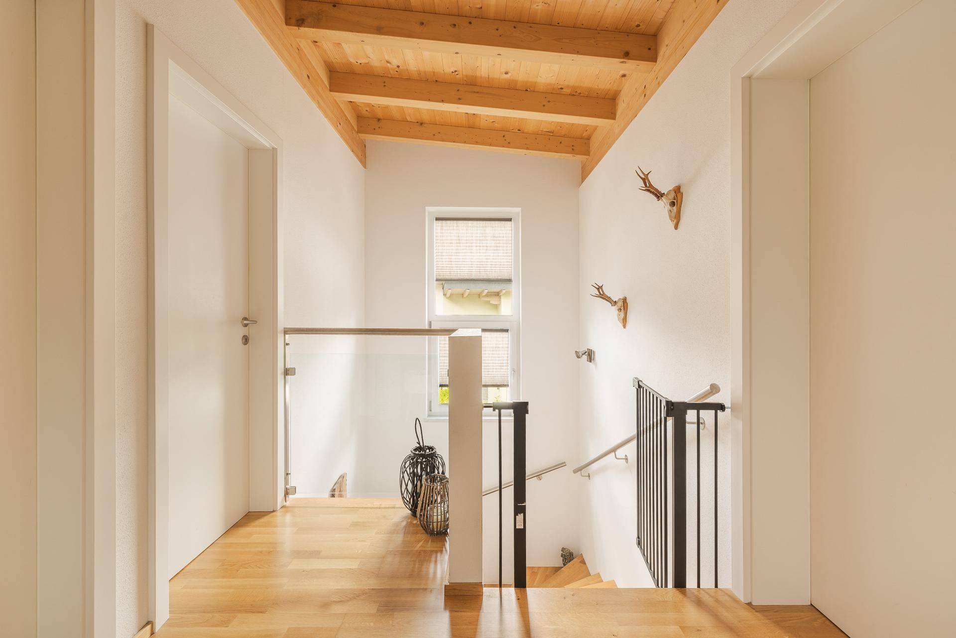 Heller Flur mit Holzdecke, Holztreppe und Glasgeländer, das für eine offene Atmosphäre sorgt.