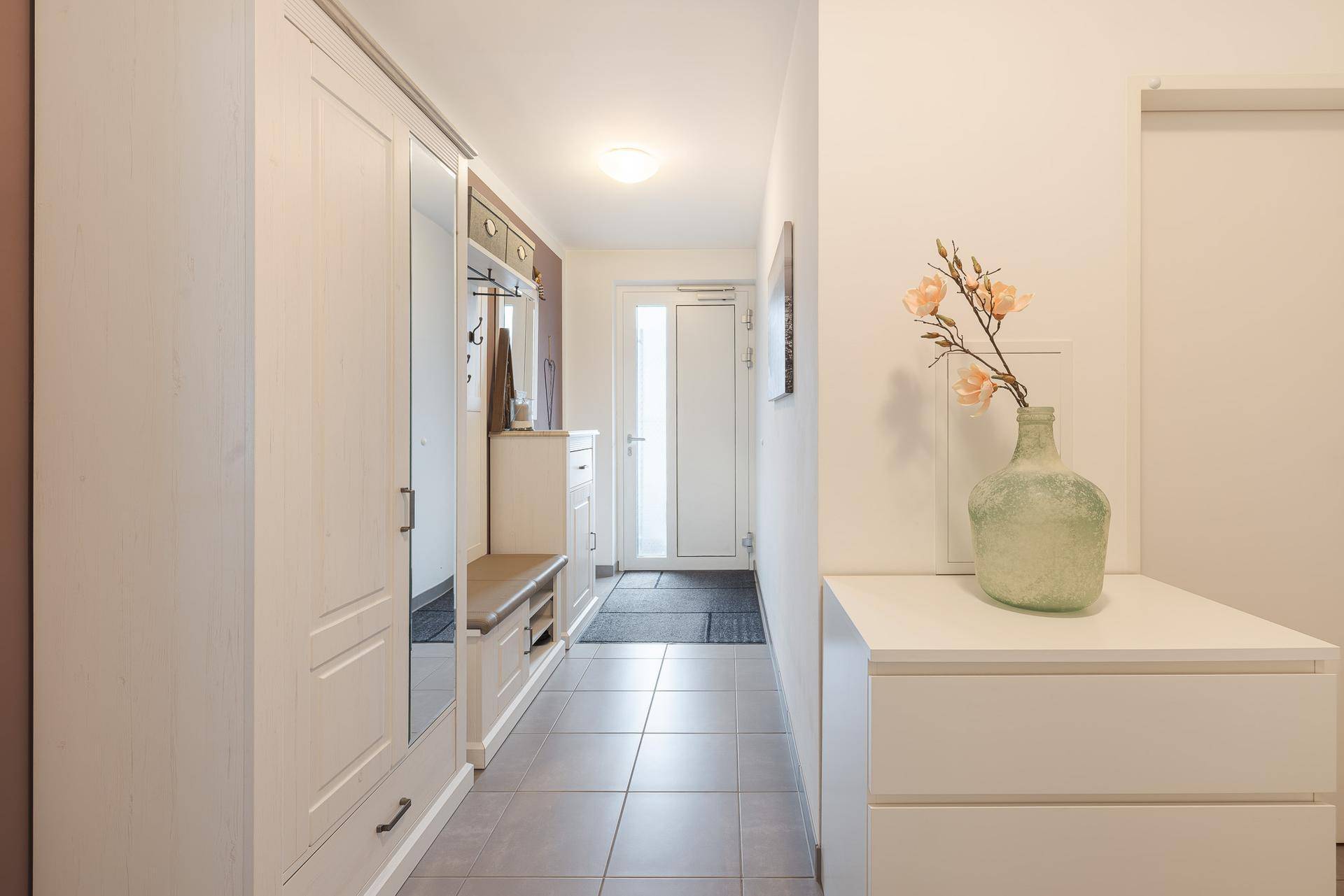 Heller Eingangsbereich mit Garderobe, Spiegel und Fliesenboden.