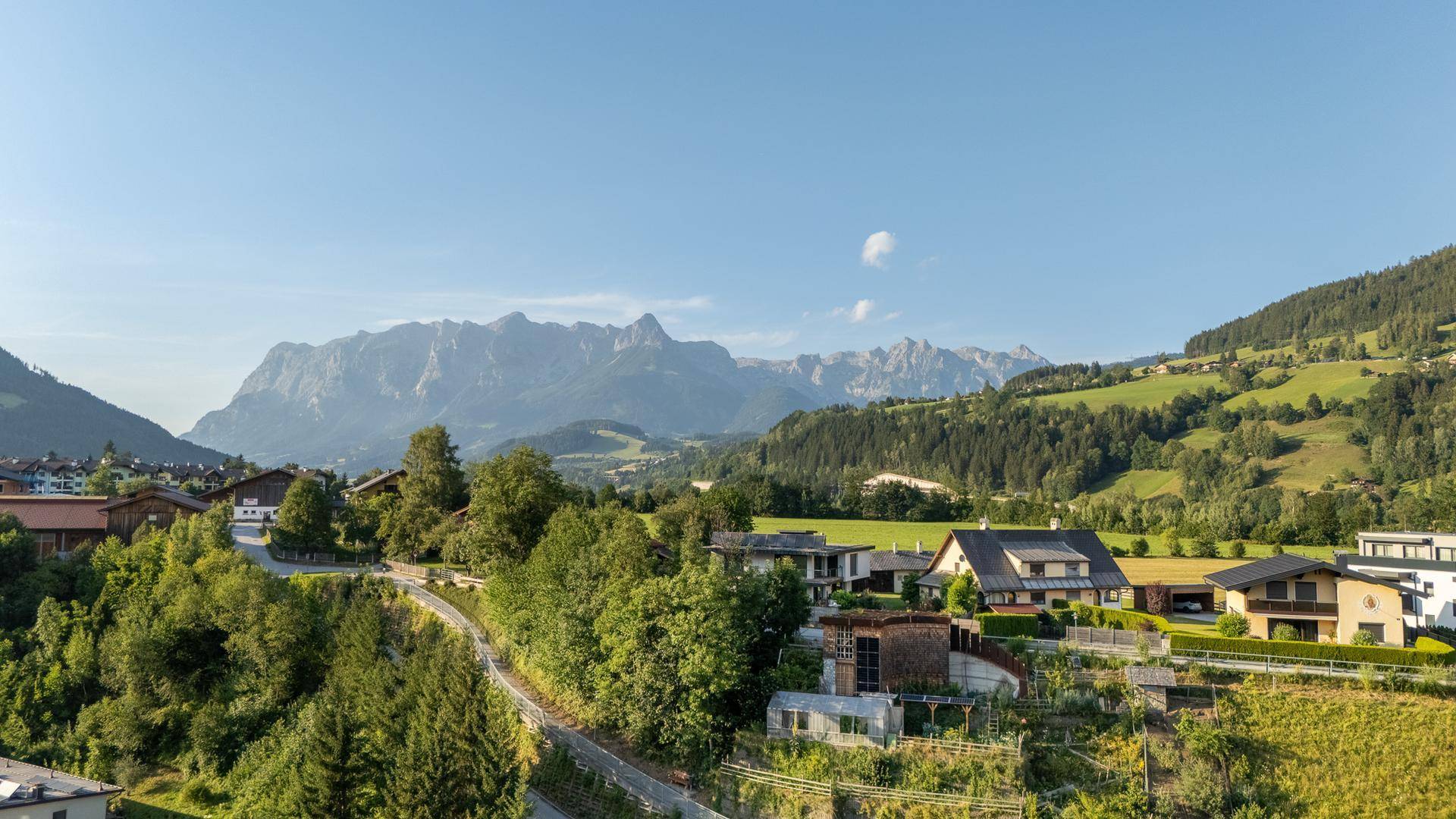 Malerische Landschaft mit Bergen, grünen Hügeln und traditionellen Häusern unter blauem Himmel.