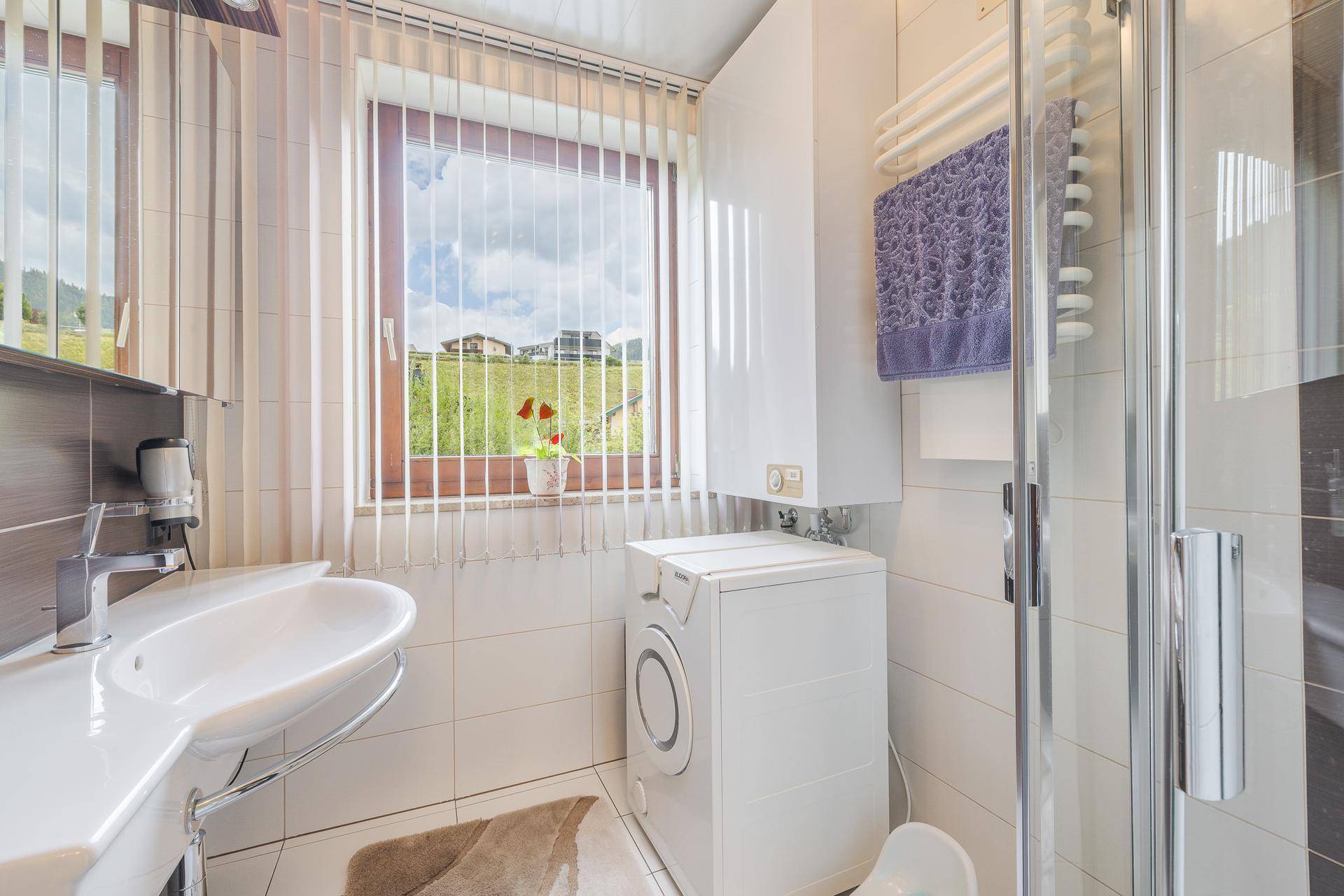 Modernes Badezimmer mit Dusche, Waschbecken, Waschmaschine und Fenster mit Bergblick.