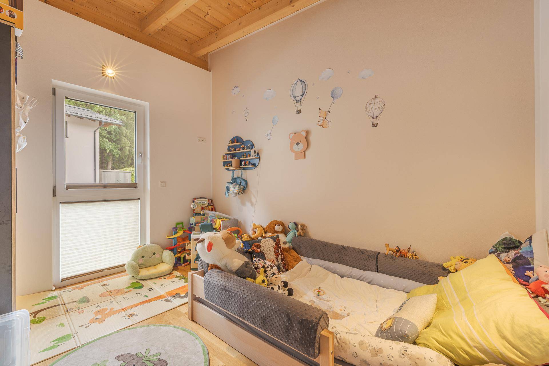 Kinderzimmer mit Holzbalkendecke, Holzboden und Spielzeug, ideal für kleine Bewohner.