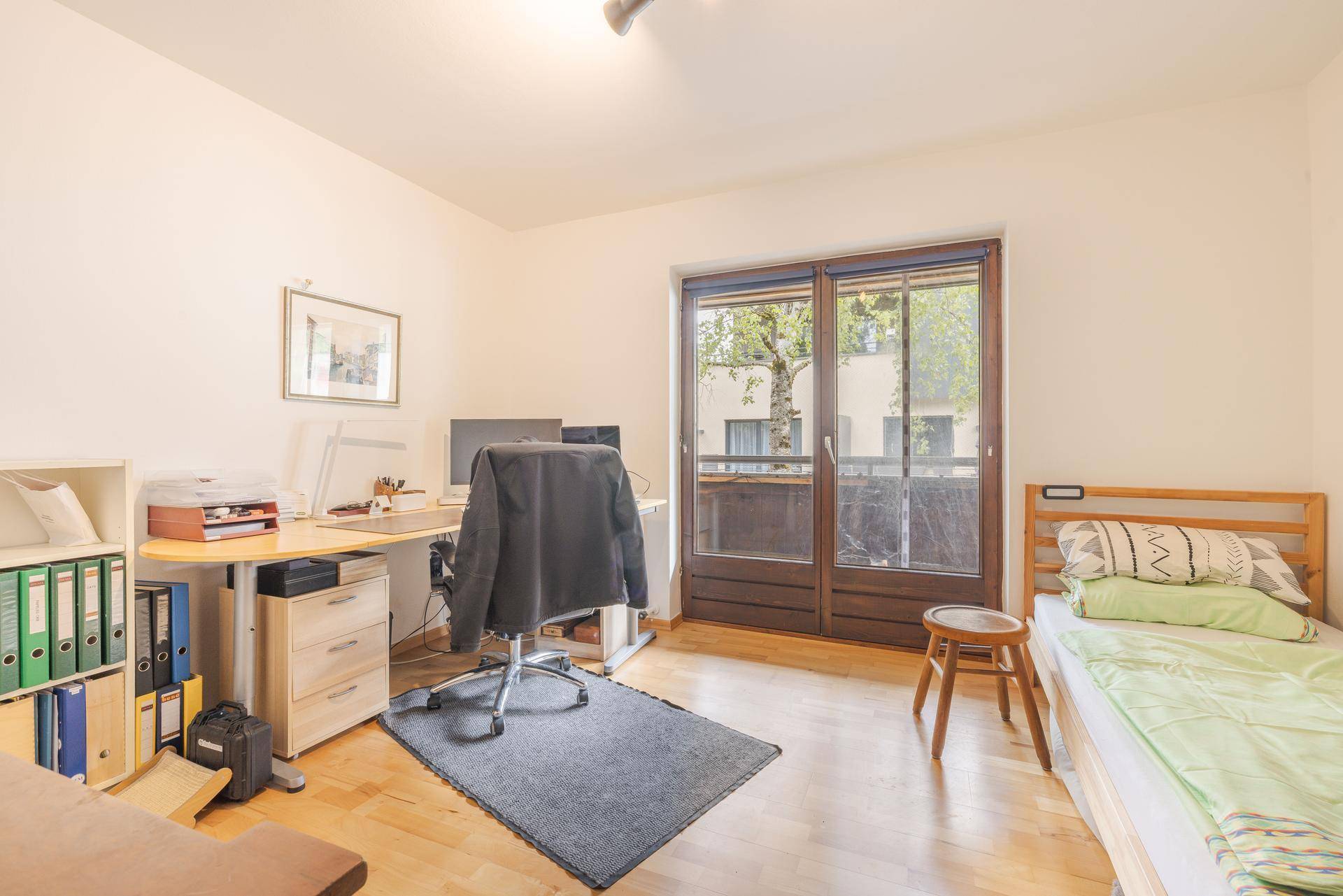 Helles Schlafzimmer mit Holzboden, Schreibtisch und direktem Zugang zum Balkon.