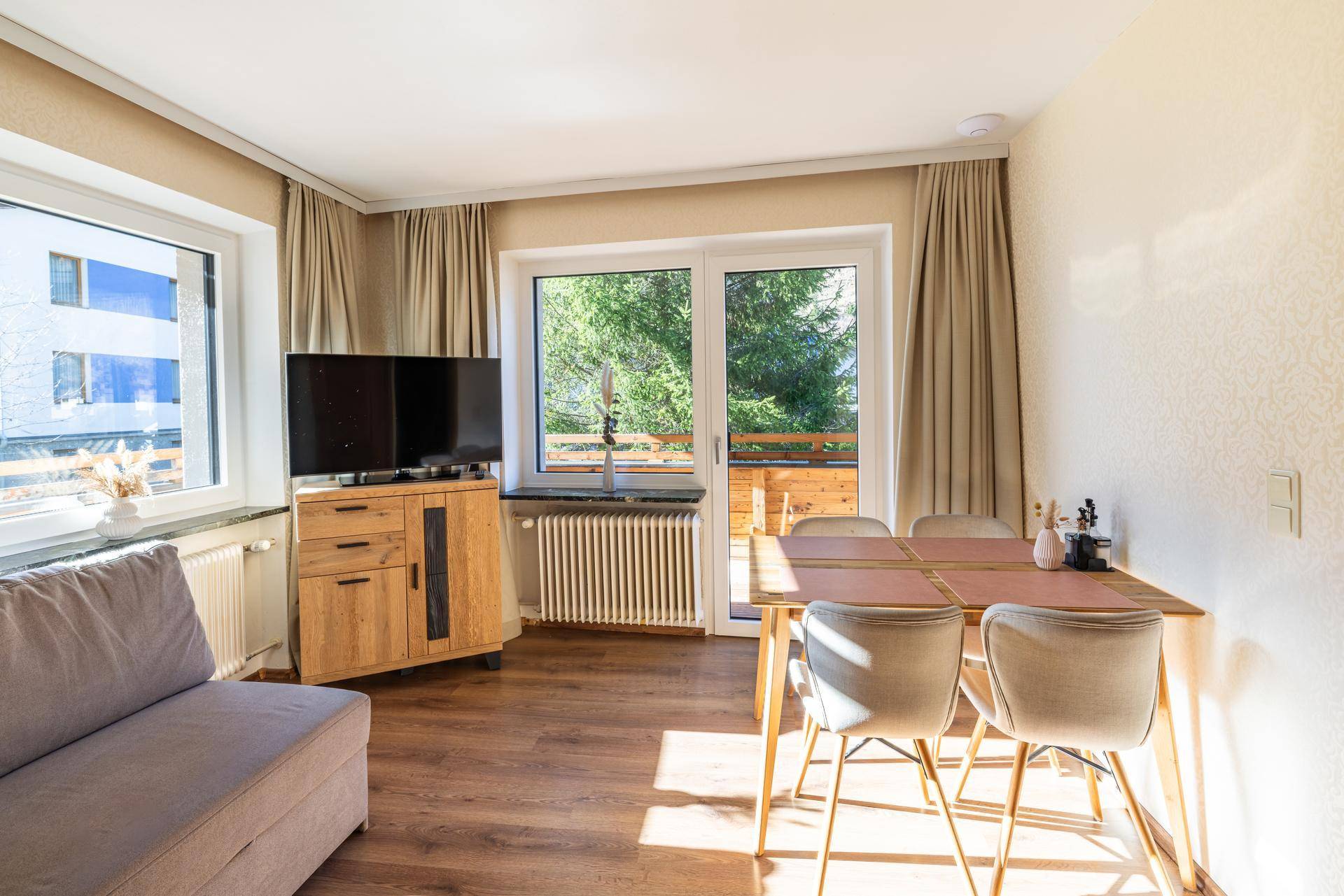 Heller Wohnbereich mit Holzboden, Esstisch und Zugang zu einem Balkon mit grüner Aussicht.