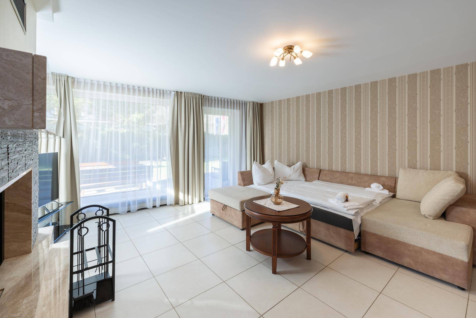Geräumiger Wohnbereich mit Fliesenboden, beigem Sofa und großen Fenstern.