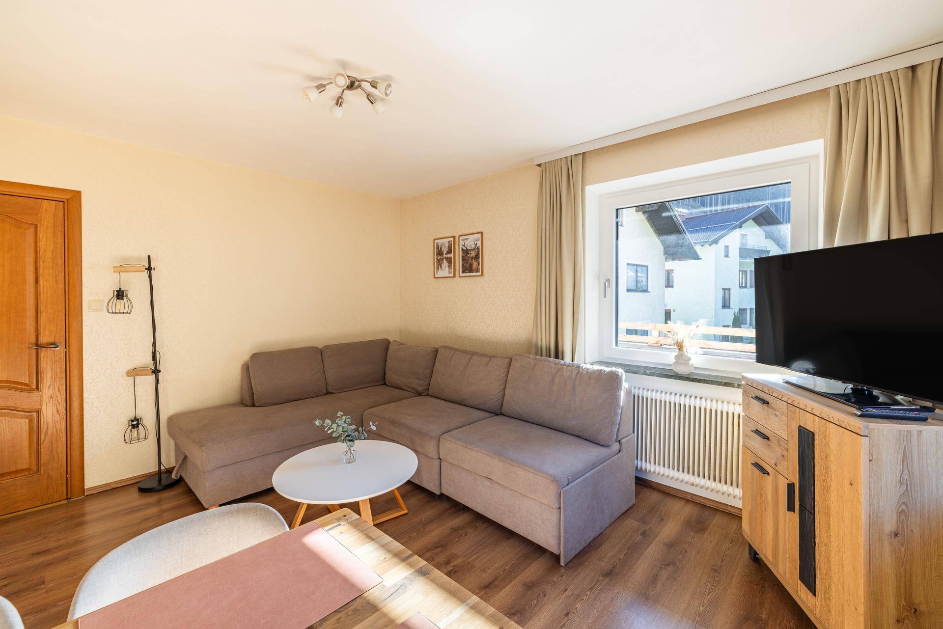 Gemütlicher Wohnbereich mit Ecksofa, Holzboden und Blick auf die umliegenden Häuser.