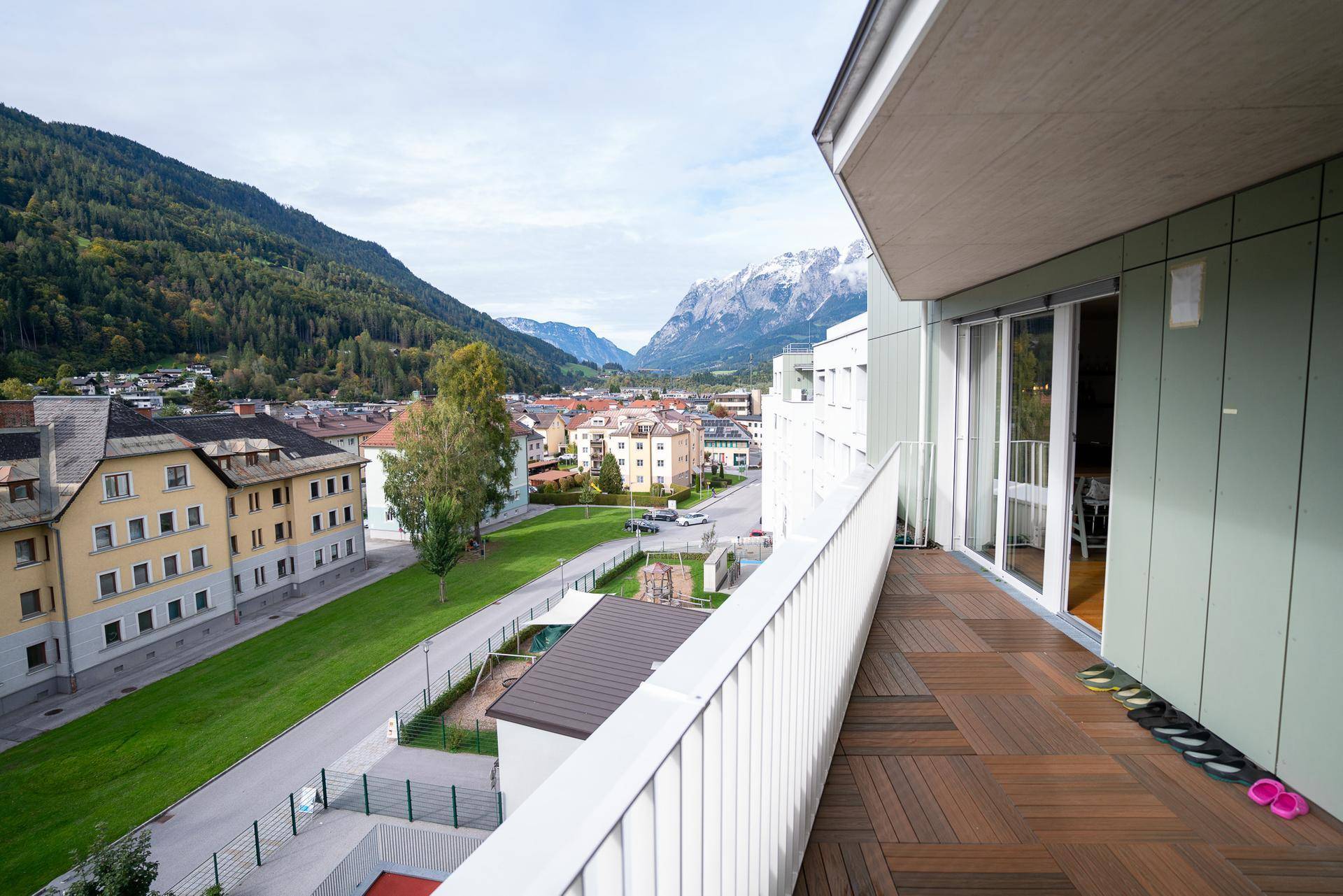 Geräumiger Balkon mit Holzboden und weitem Blick über die Stadt und die Alpen.