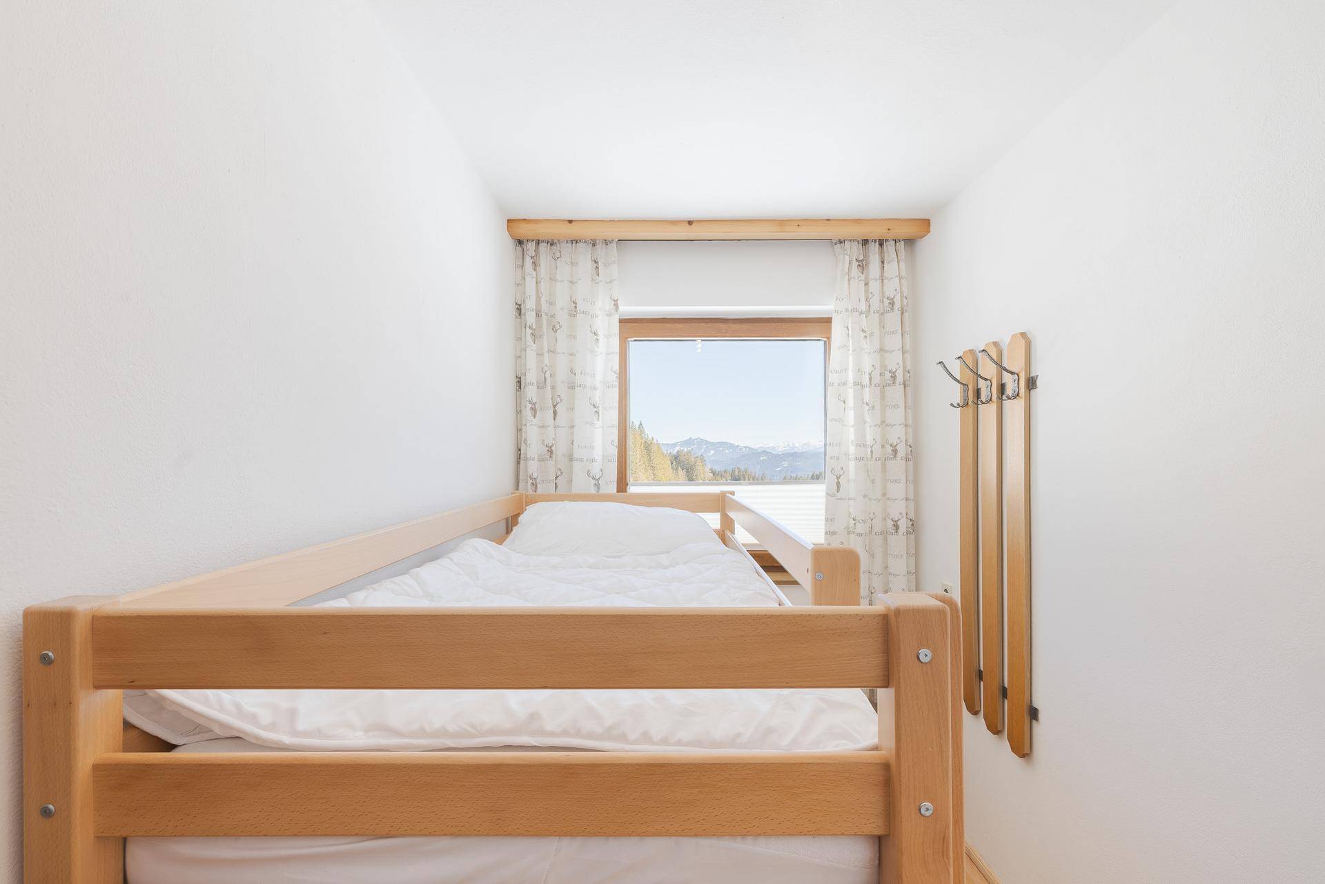 Kleines Schlafzimmer mit Etagenbett, weiß gestrichenen Wänden und Bergblick aus dem Fenster.