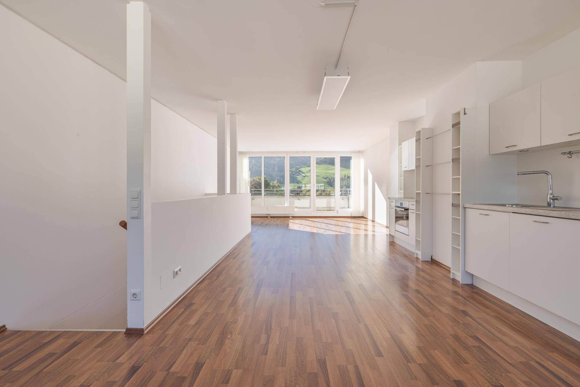 Geräumiger, offener Wohnbereich mit integrierter Küche, Laminatboden und viel Tageslicht.