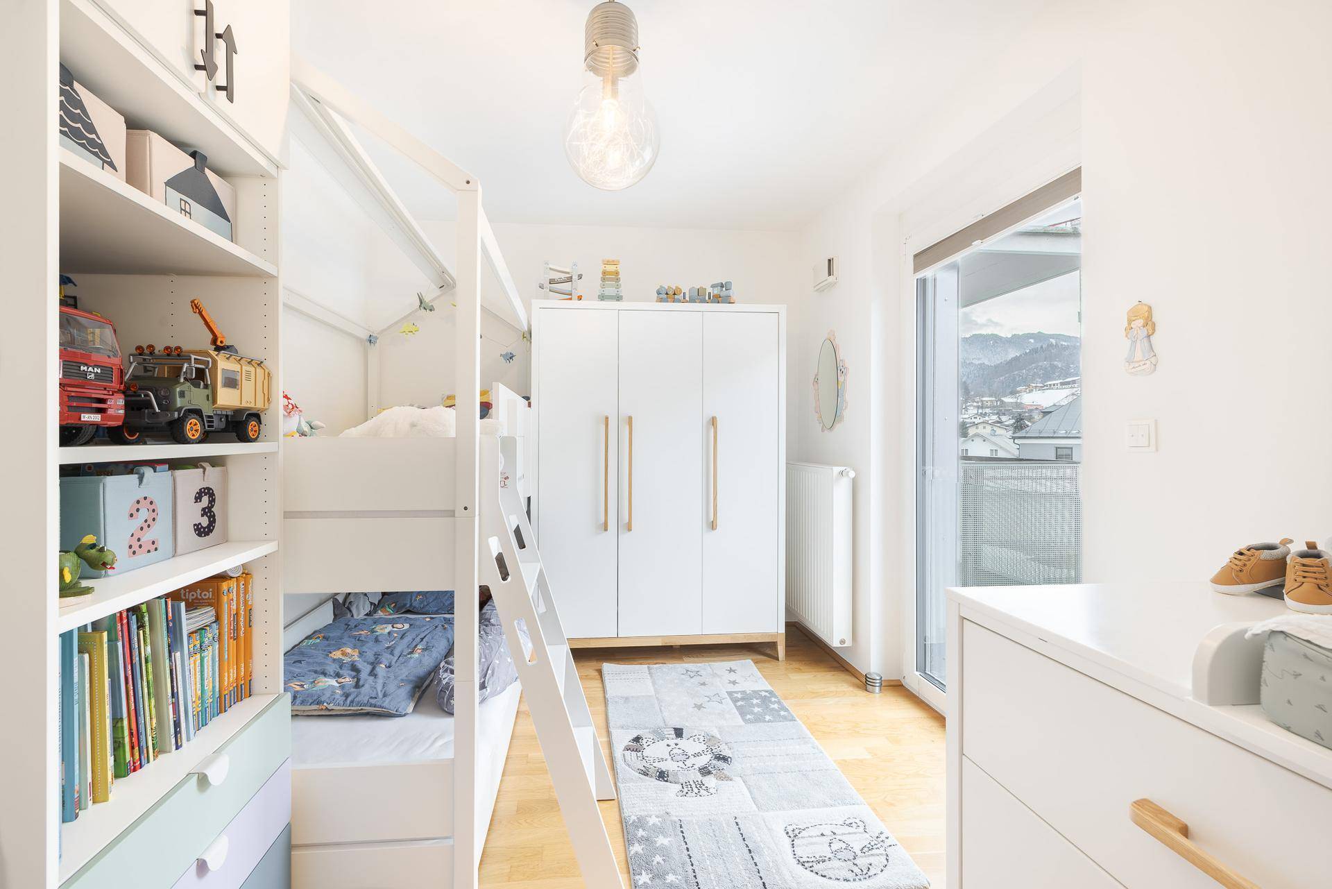 Kinderzimmer mit Etagenbett, Spielzeugregal und viel Tageslicht.