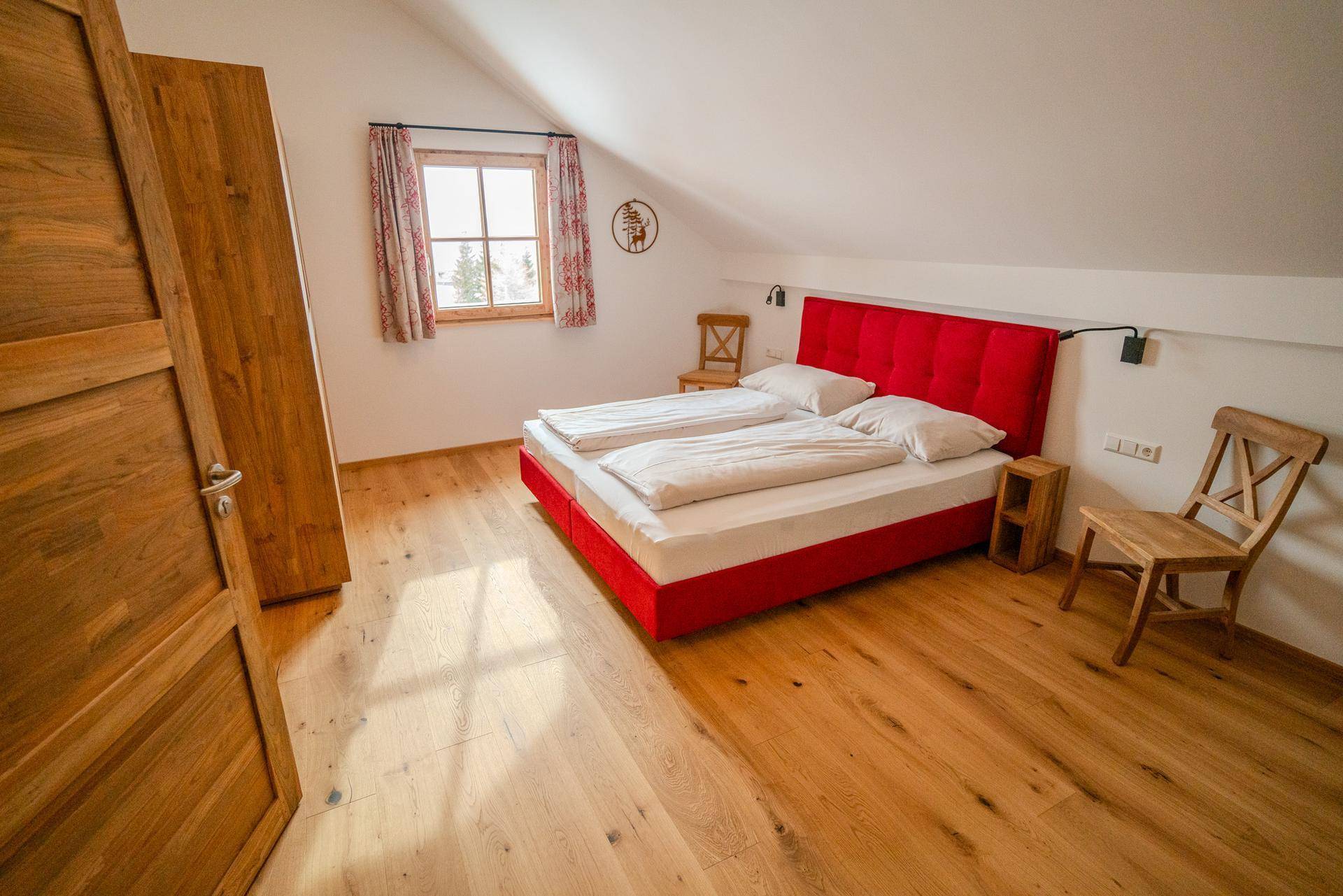 Helles Schlafzimmer mit rotem Doppelbett, Holzboden und Dachschräge, bietet eine gemütliche Rückzugsmöglichkeit.
