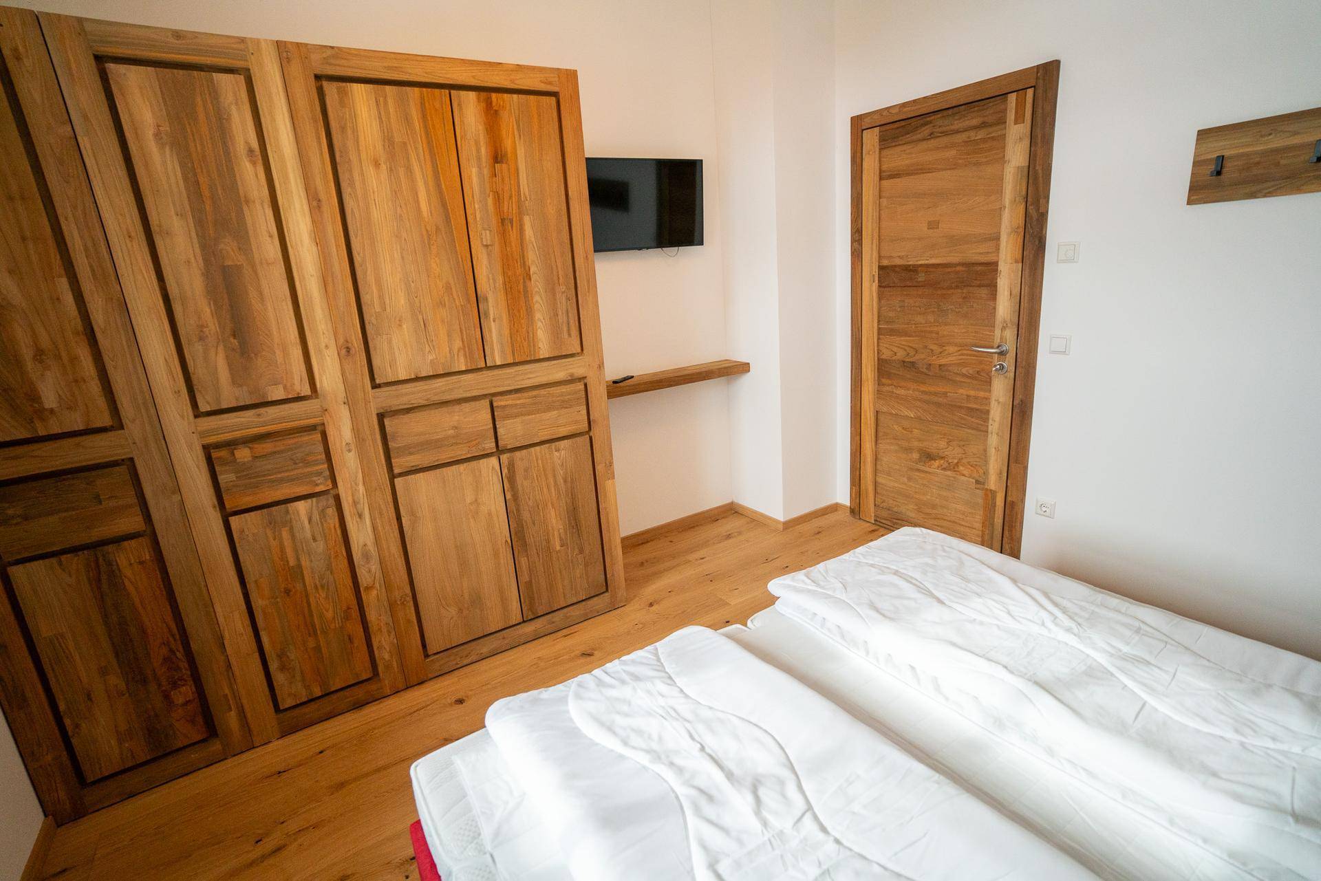 Schlafzimmer mit großem Holzschrank, Fernseher und Holztür, bietet praktischen Stauraum und Komfort.