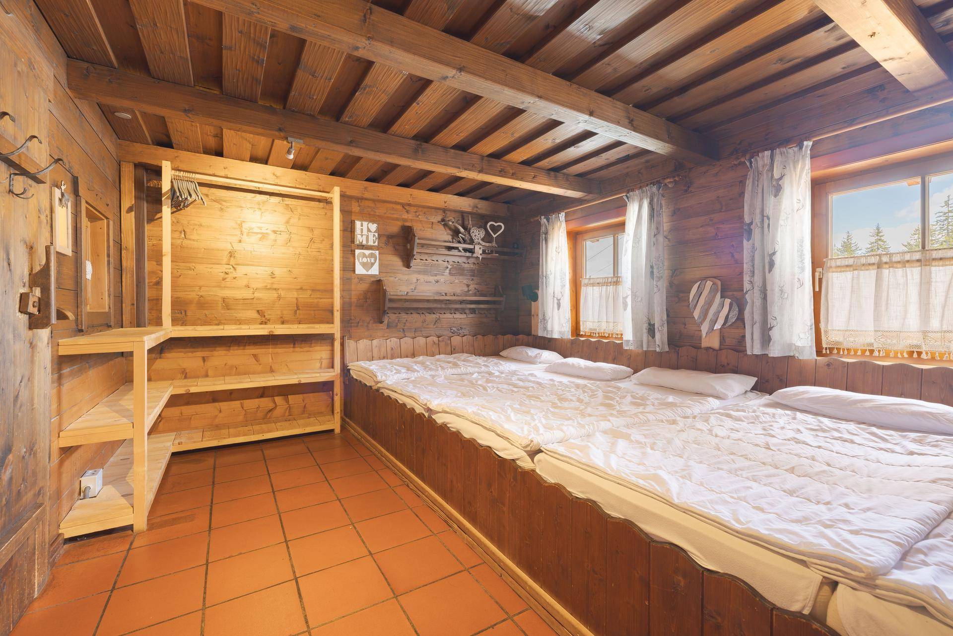 Gemütliches Schlafzimmer mit mehreren Betten in Holzrahmen, Holzwänden und Terrakottafliesen, sowie offenem Kleiderschrank.