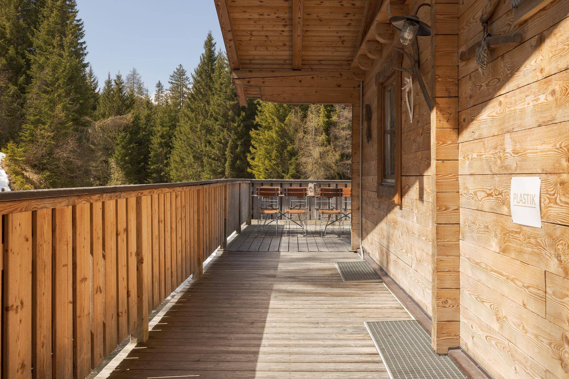 Holzverkleideter Balkon mit rustikalem Geländer und Blick auf die umliegende Natur, unter strahlendem Sonnenschein.