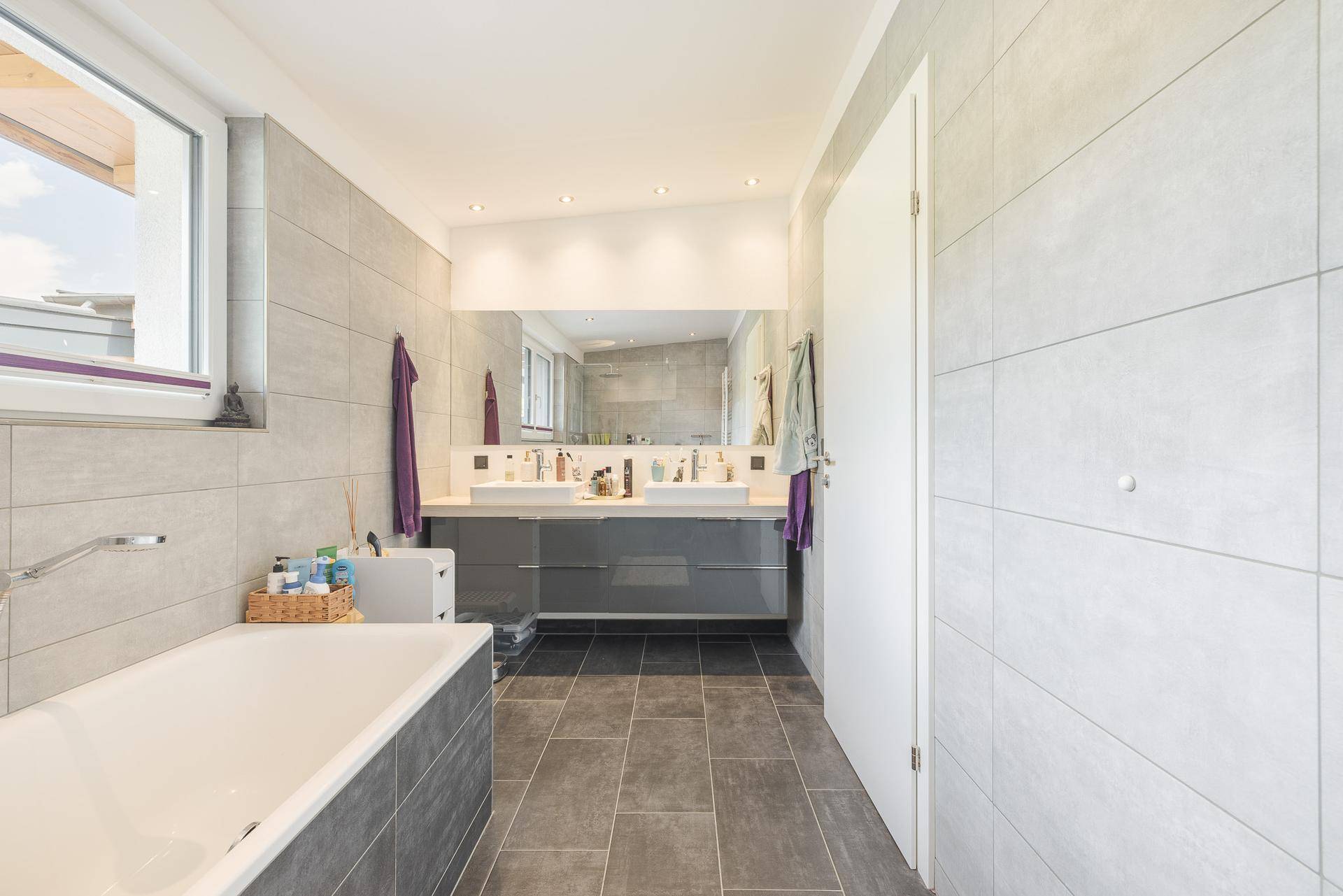 Modernes Badezimmer mit Doppelwaschbecken, Badewanne und großen Fliesen, sehr geräumig.