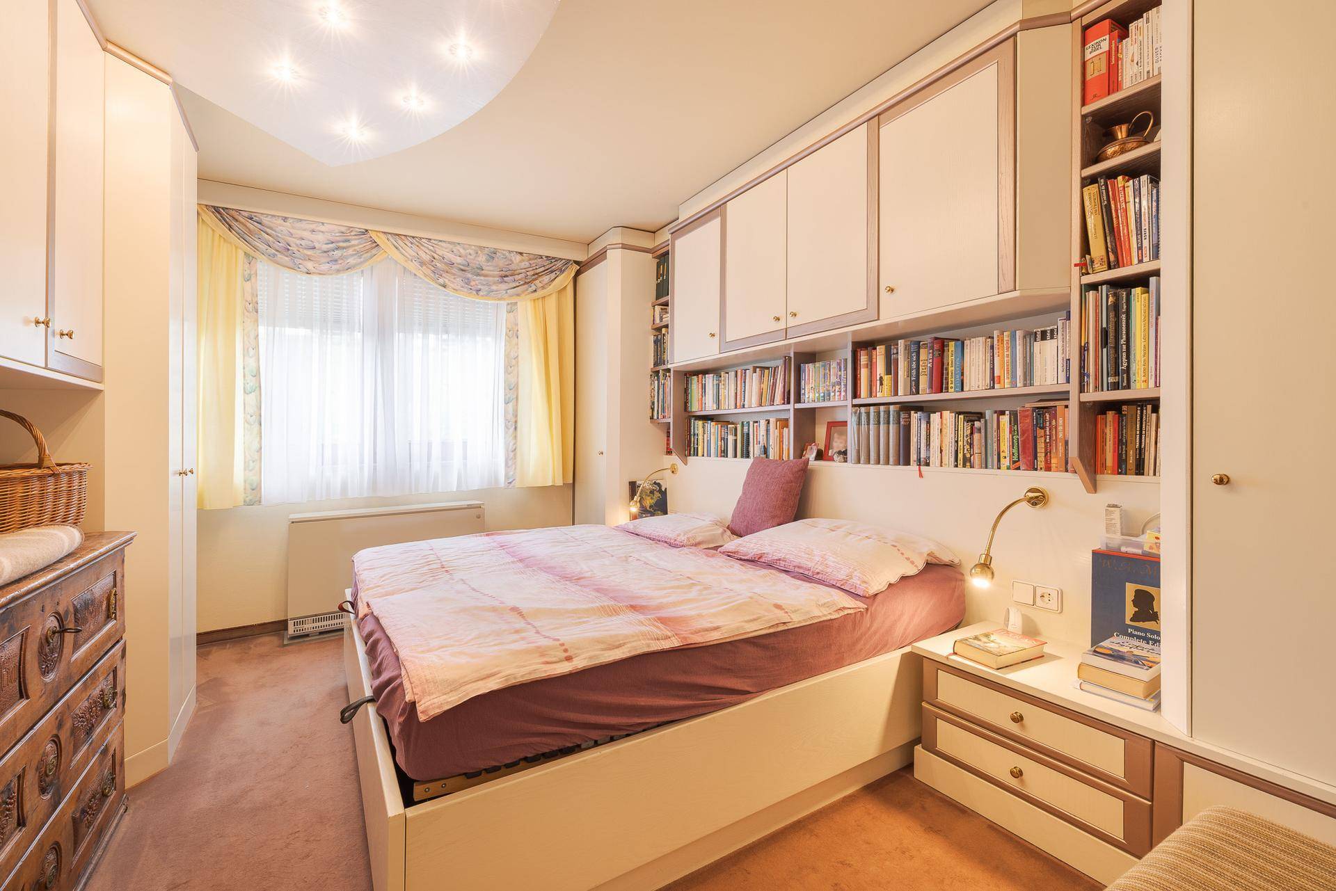 Schlafzimmer mit Doppelbett, integrierten Bücherregalen und Teppichboden, hell und funktional.