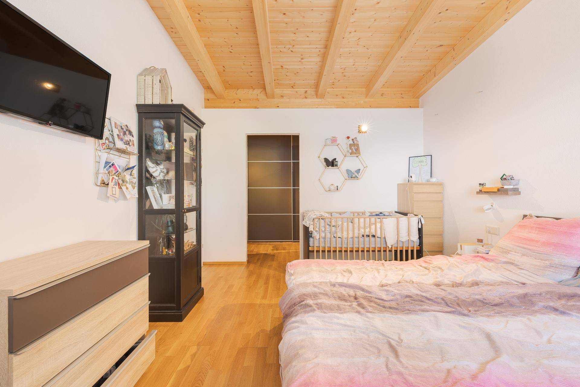 Schlafzimmer mit Holzbalkendecke, Holzboden und Babybett, bietet eine ruhige Schlafumgebung.