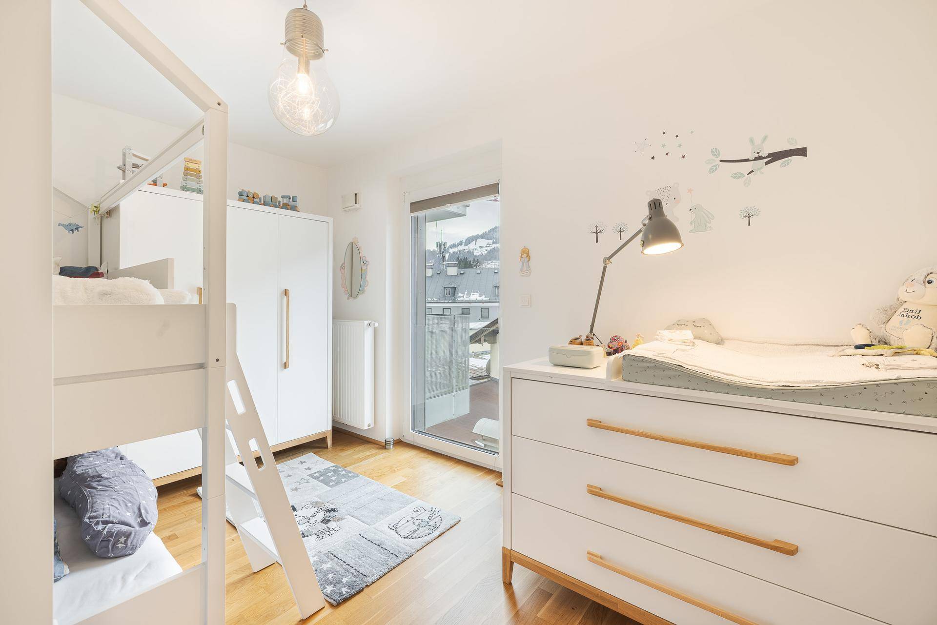 Helles Kinderzimmer mit Etagenbett, Wickeltisch und Zugang zum Balkon.