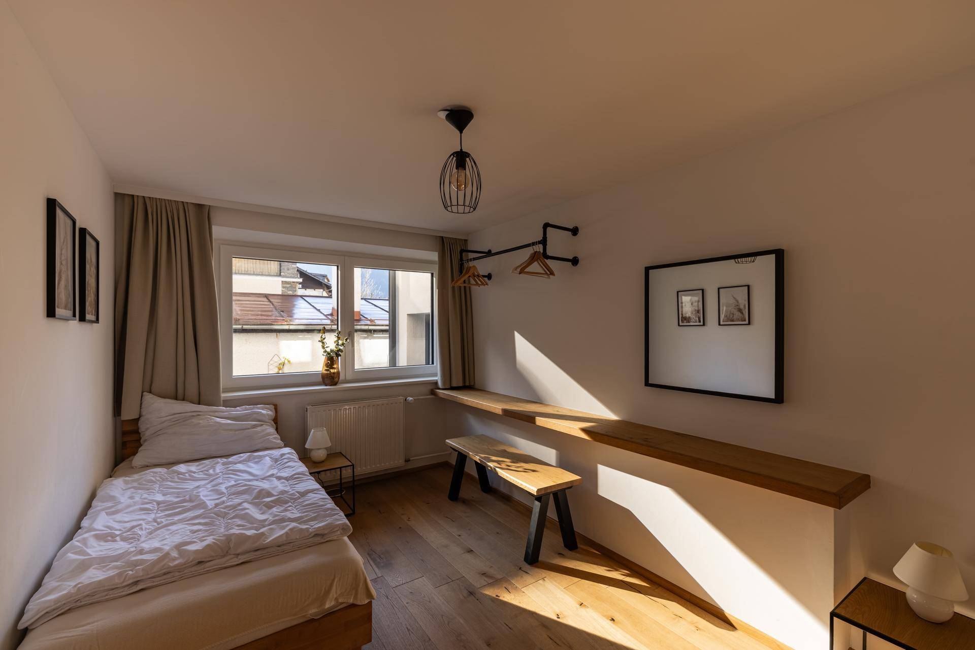 Helles Einzelzimmer mit Holzboden, Fenster und minimalistischer Einrichtung.