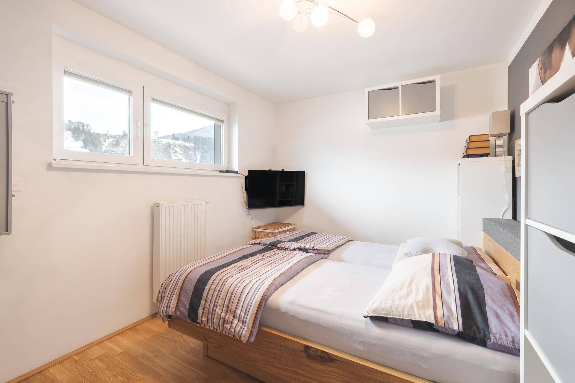 Gemütliches Schlafzimmer mit Doppelbett, Holzboden und Bergblick durch die Fenster.