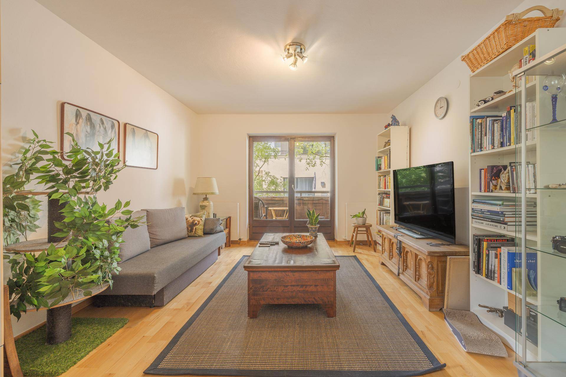 Helles Wohnzimmer mit Holzboden, bequemer Couch und Zugang zu einem kleinen Balkon.