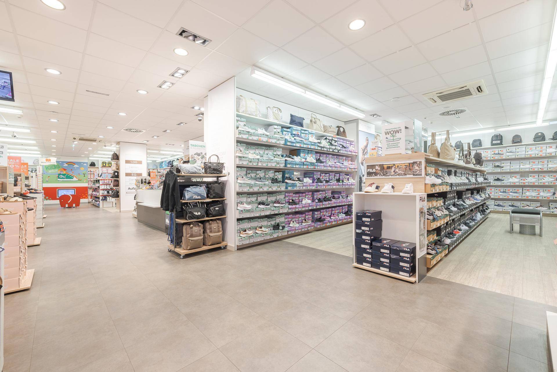Moderner Schuhladen mit breiten Gängen und gut sortierten Regalen für verschiedene Produkte.