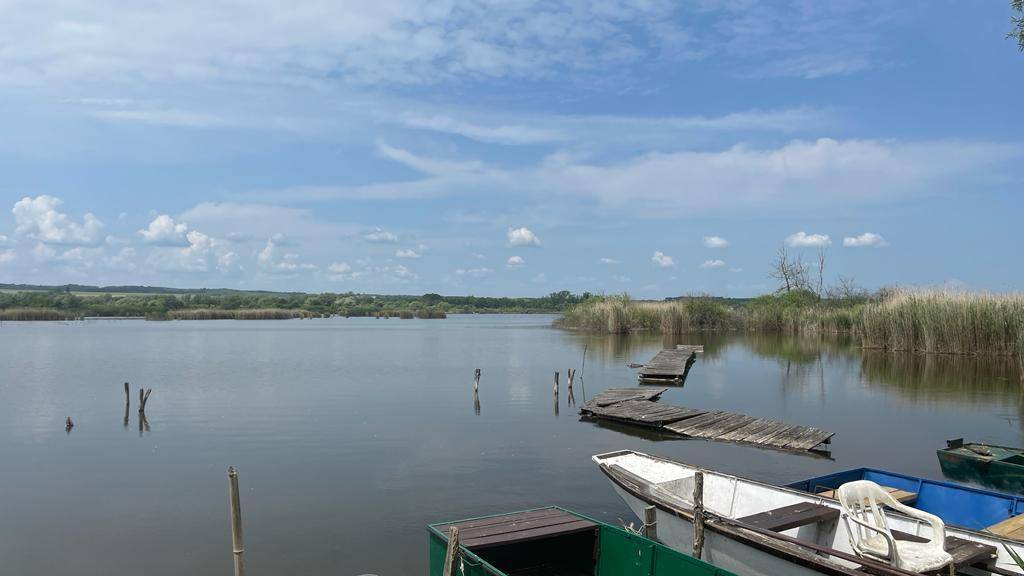 Weitläufiger See mit Booten und verfallenen Holzstegen unter einem weiten, blauen Himmel.