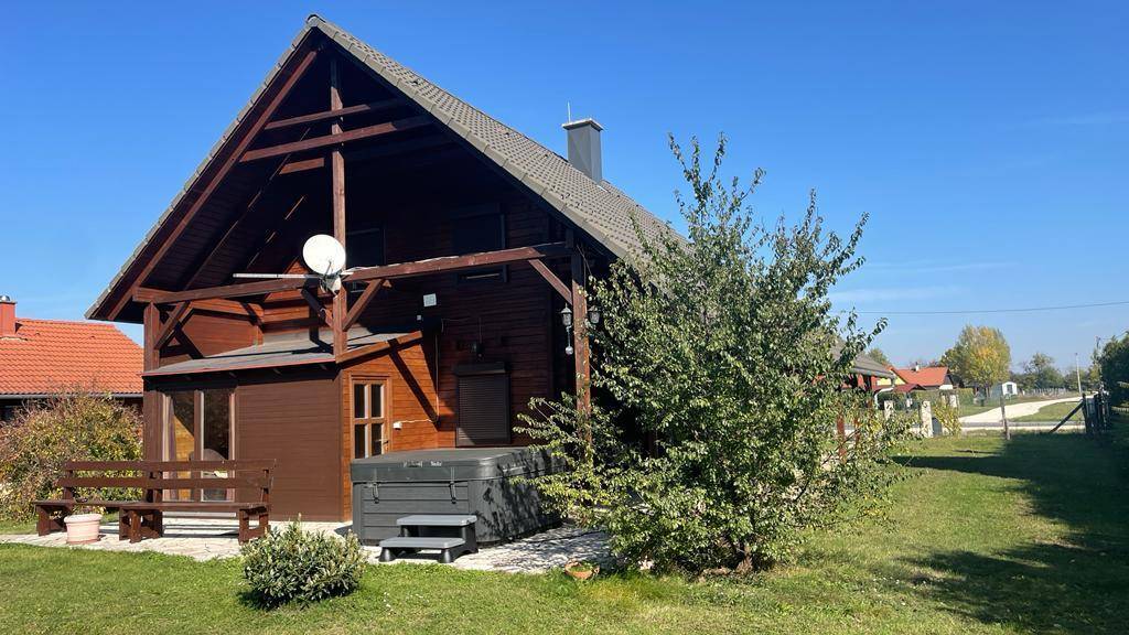 Ansicht des Holzhauses mit Whirlpool und gepflegtem Rasen, umgeben von Büschen.
