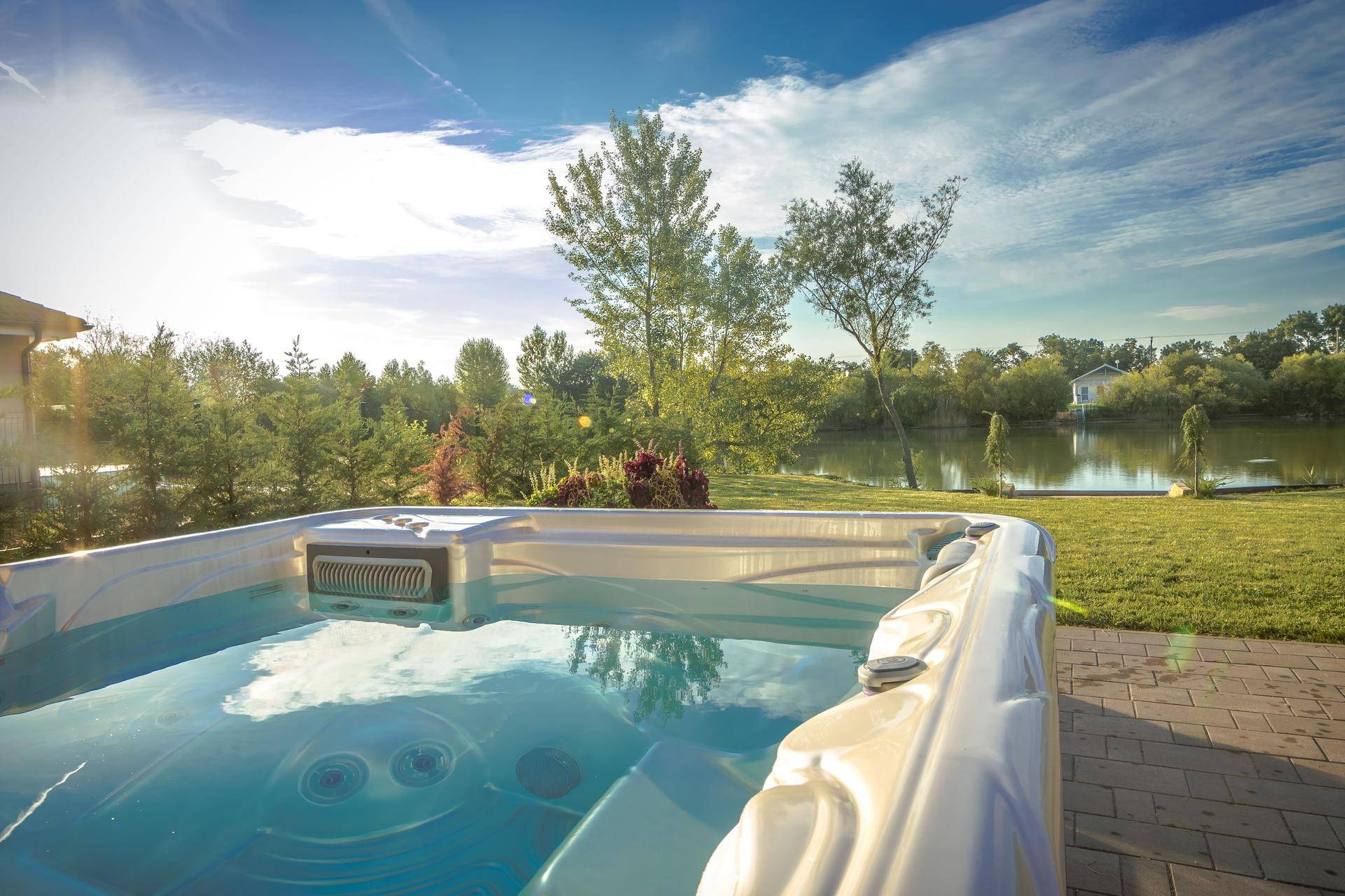 Außenwhirlpool im Garten mit Seeblick unter strahlend blauem Himmel.