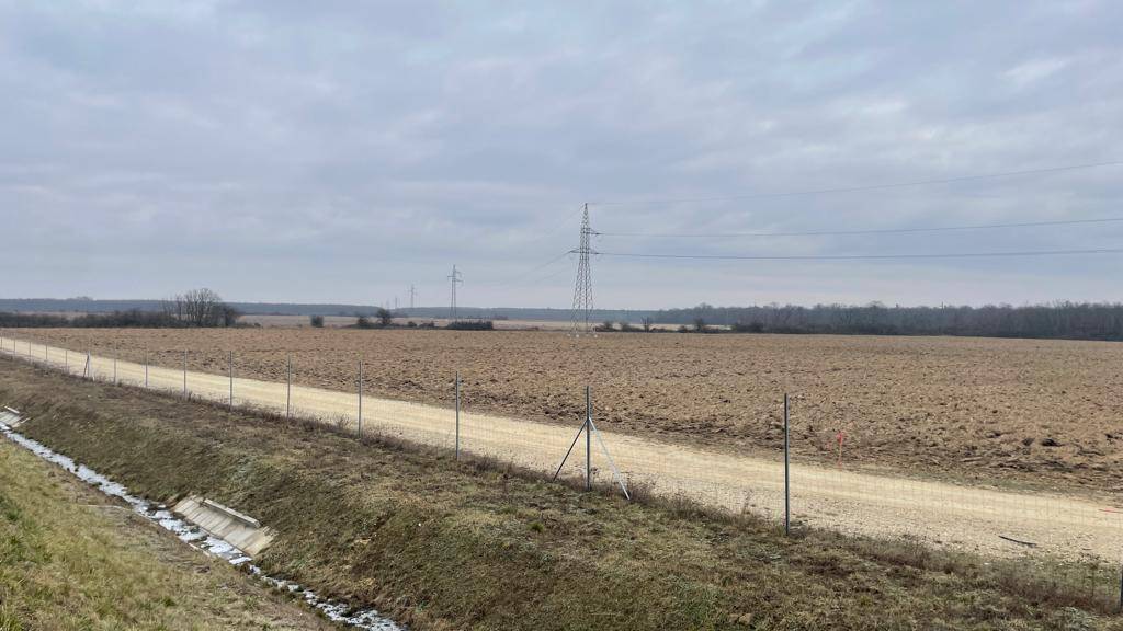 Autobahn neben weiten Feldern mit Stromleitungen und einem Entwässerungsgraben.