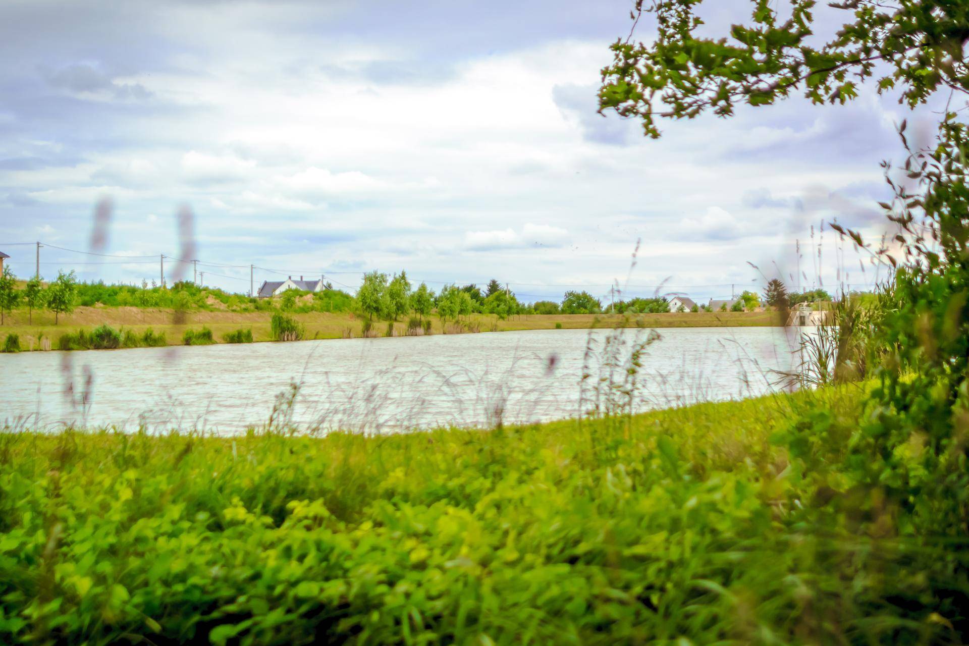 Weitläufiger See mit grünen Ufern und Häusern in der Ferne unter bewölktem Himmel.