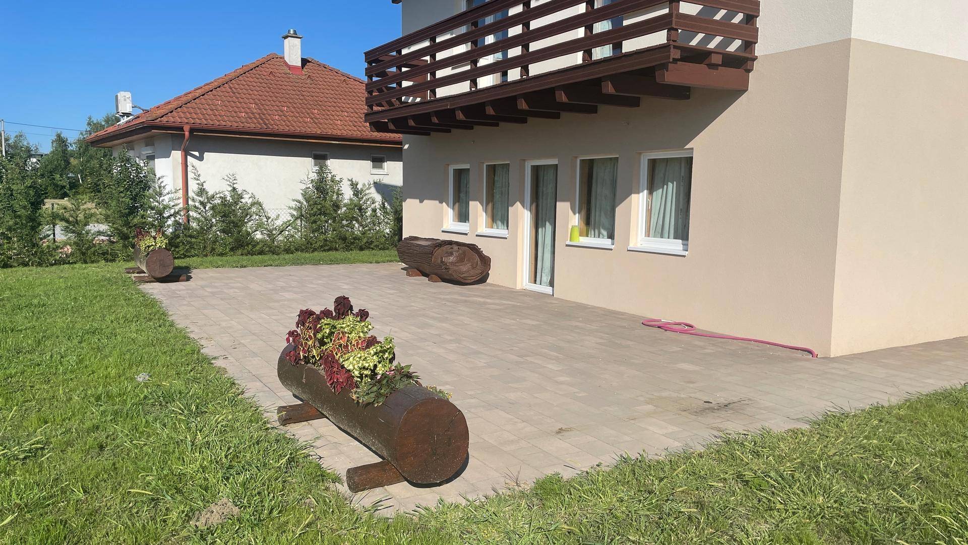 Gepflasterte Terrasse mit Blumenkübeln und Rasenfläche neben dem Haus.