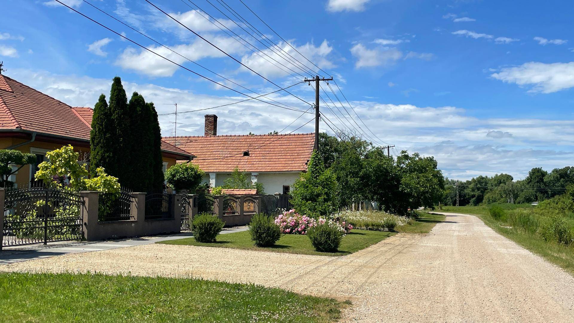 Ländliche Straße mit traditionellen Häusern, umgeben von grüner Natur und blauem Himmel.